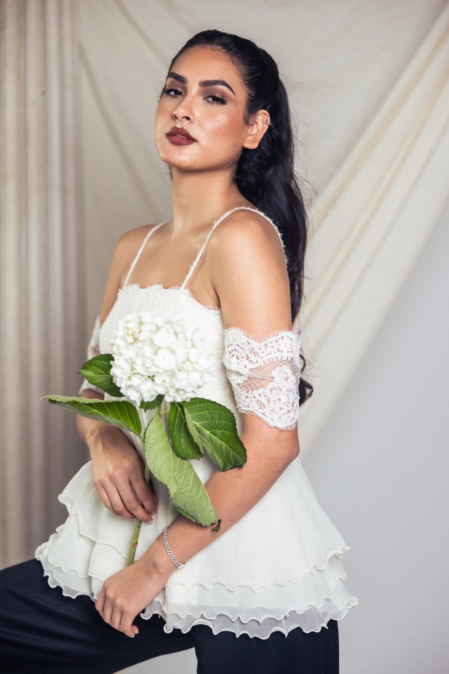 Model in beautiful off-white dress in a studio setting with a hydrangea