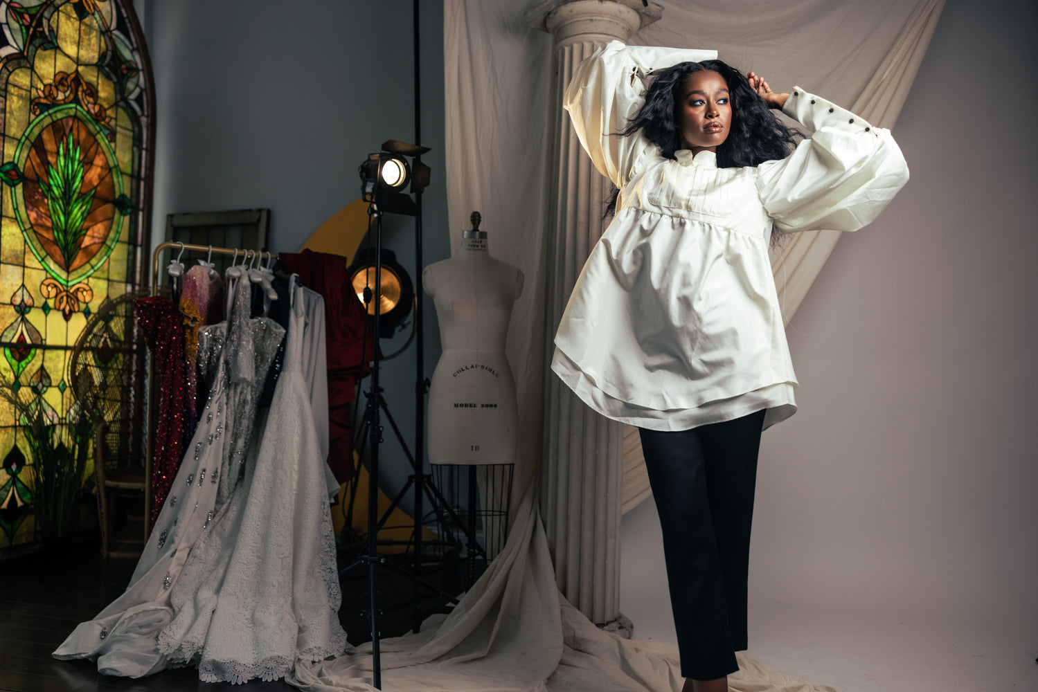 Model in voluminous ruffled blouse and skinny black pants in a studio setting