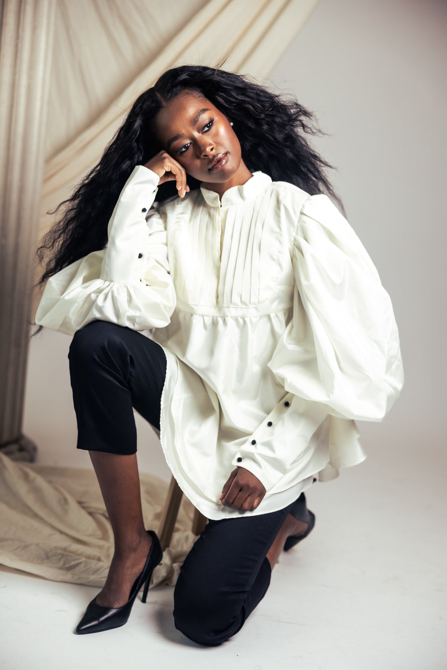 Model in voluminous ruffled blouse and skinny black pants in a studio setting