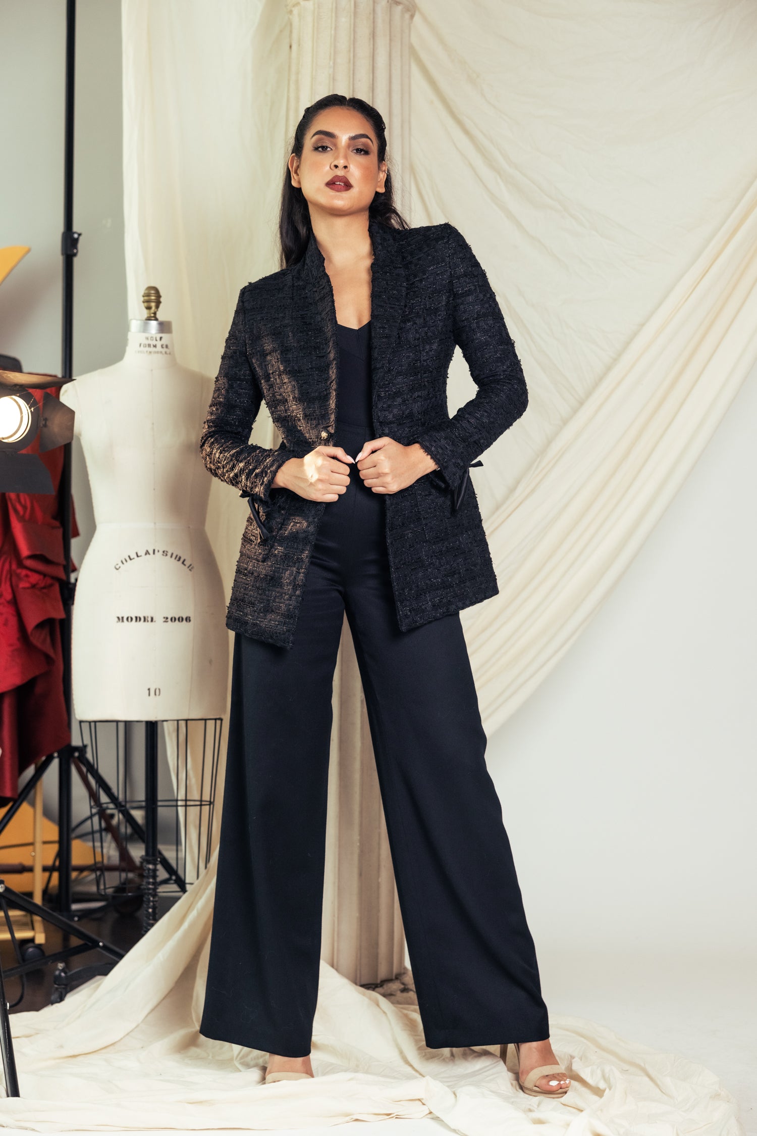 Woman in a black tweed blazer and wide-leg black pants in a studio setting