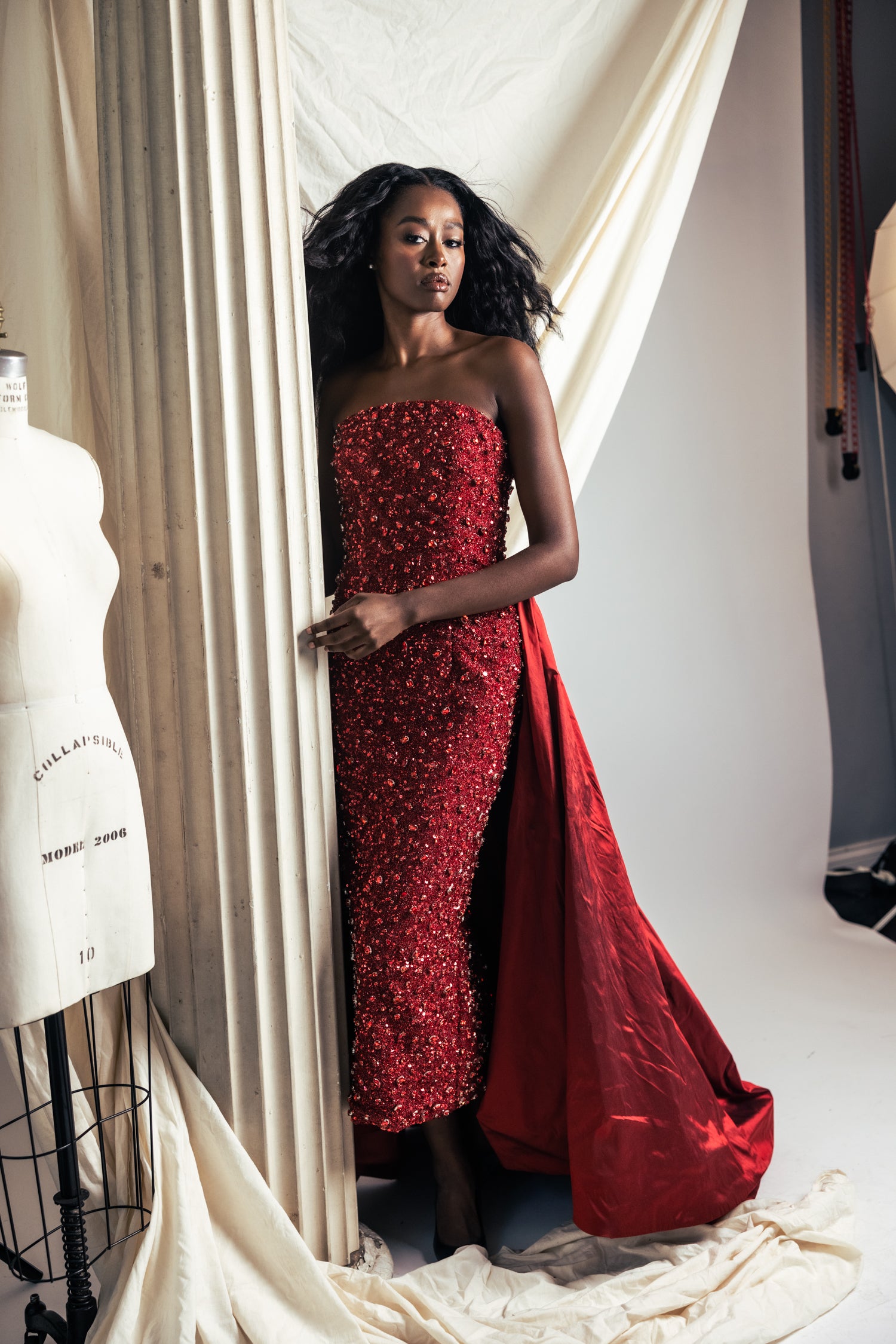 Woman in a red strapless gown standing in a studio setting.