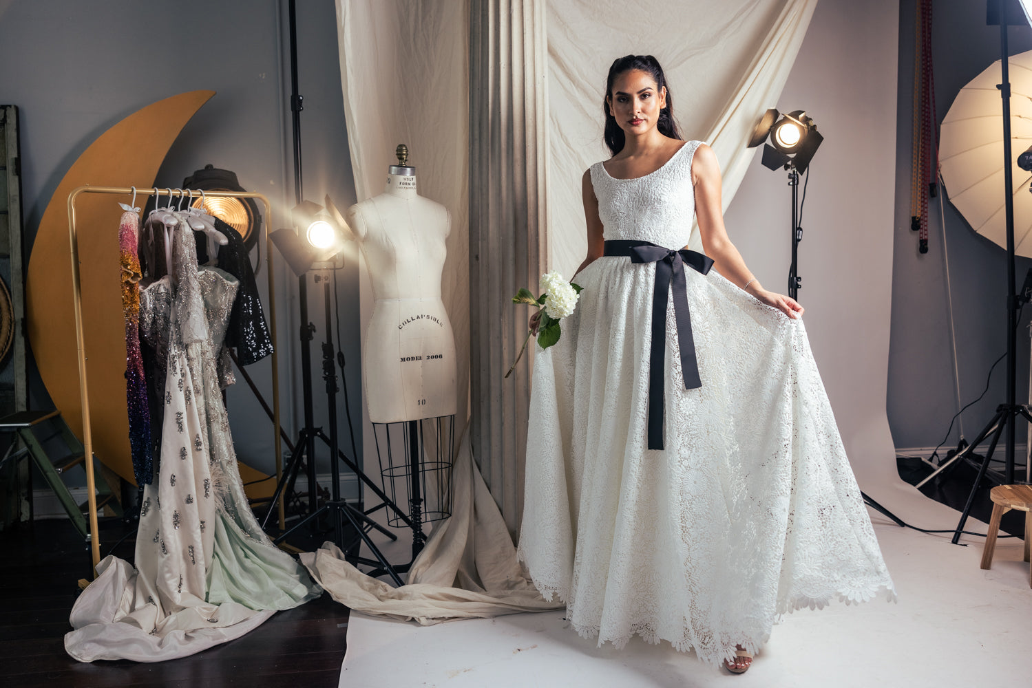 Woman in a white dress with a black belt standing in a studio setting.