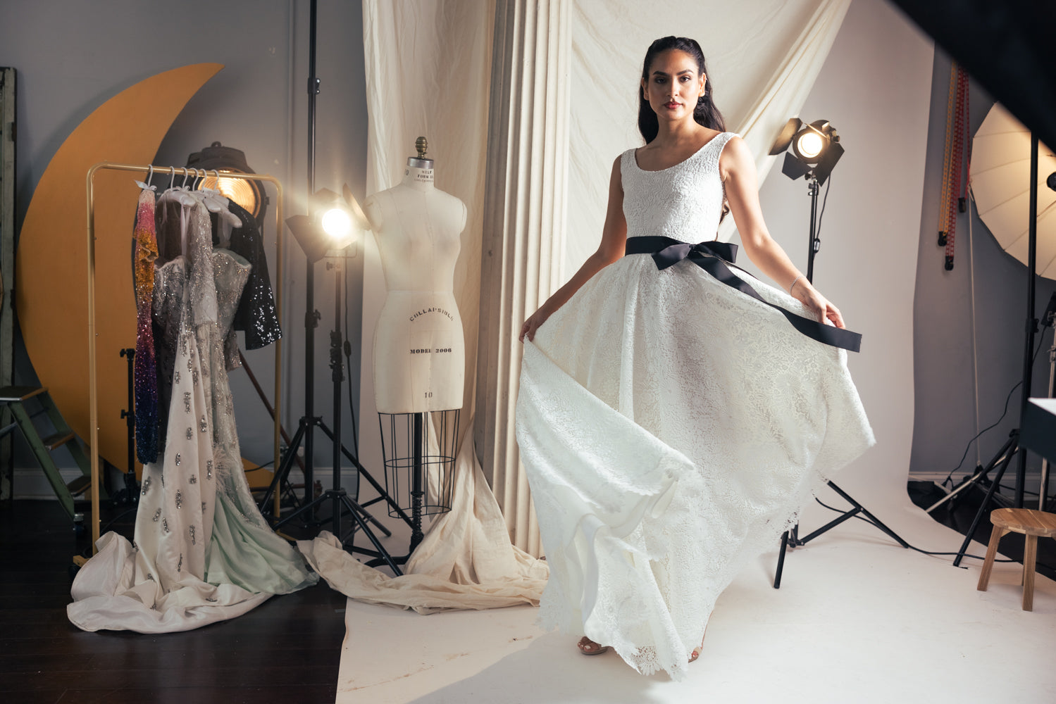 Woman in a white dress with a black belt standing in a studio setting.