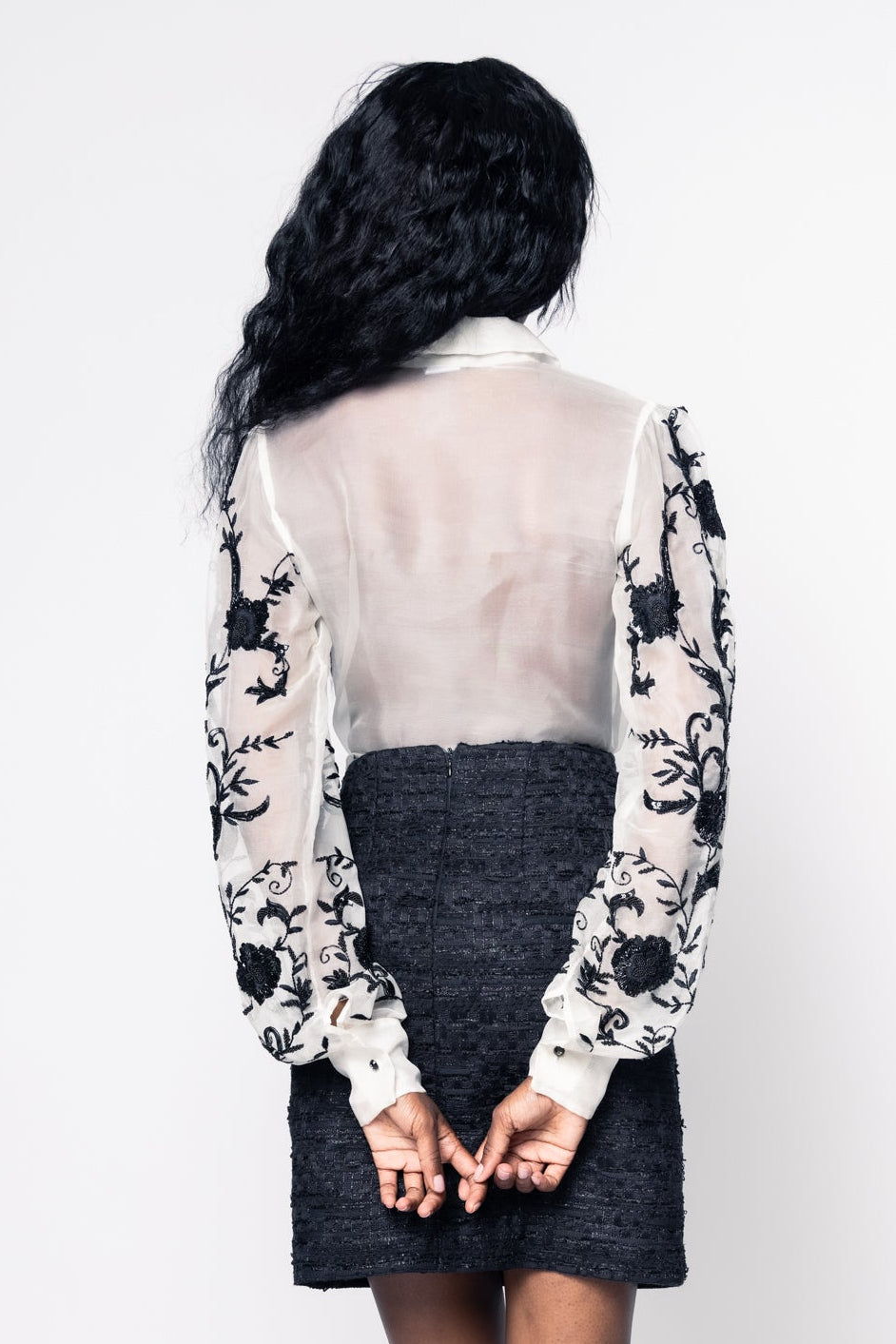 Person wearing a floral blouse with sheer sleeves and a black skirt on a white background