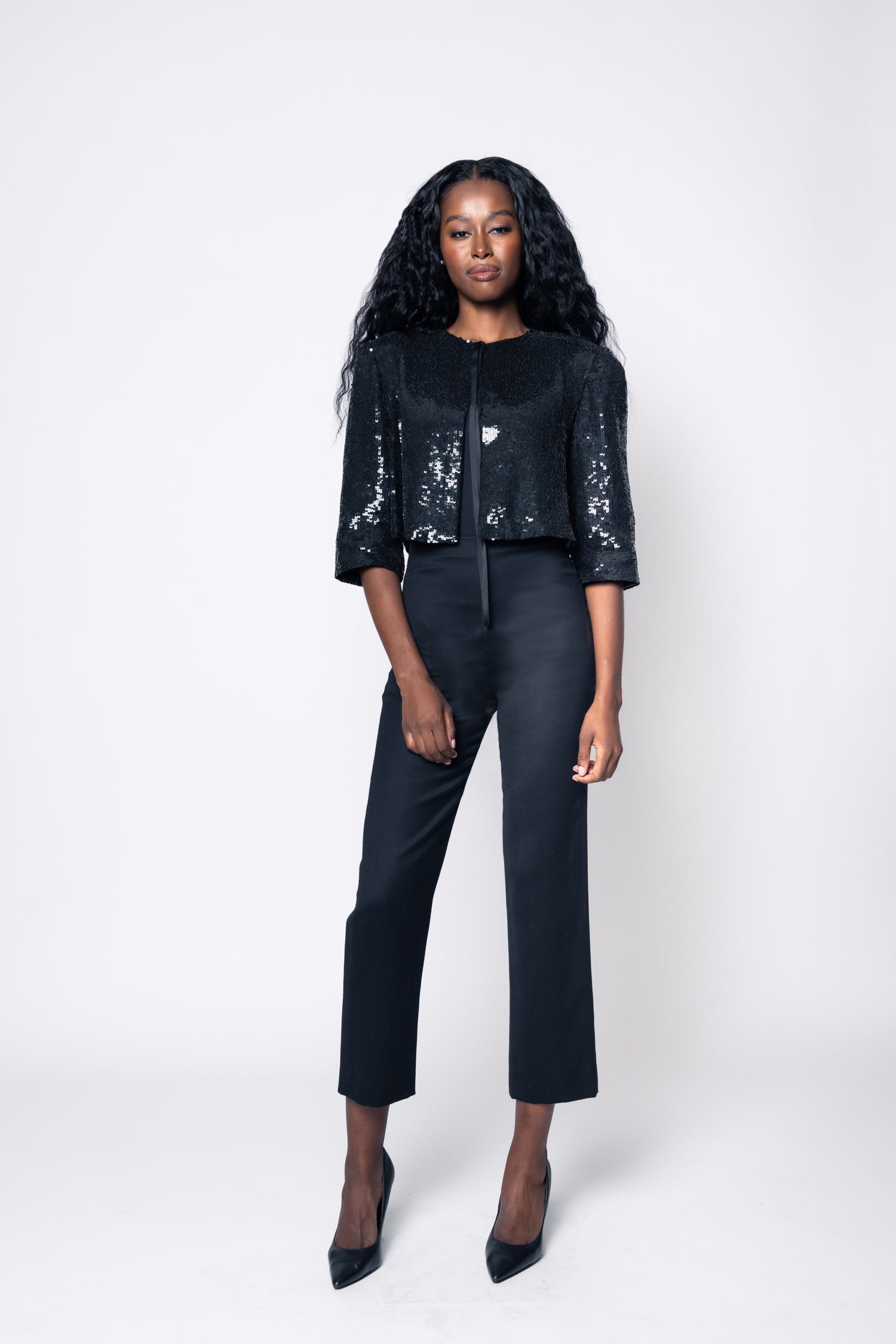 Woman wearing a black sequin jacket and black pants on a white background