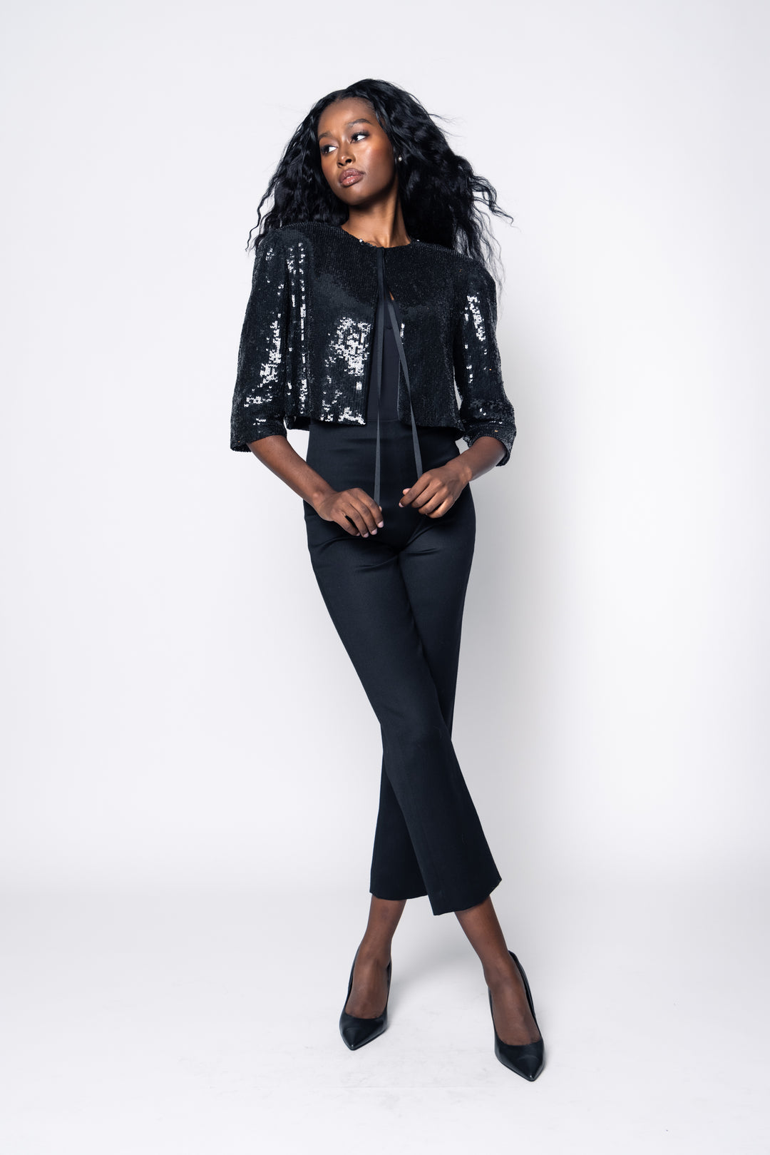 Woman wearing a black sequin jacket and black pants on a white background