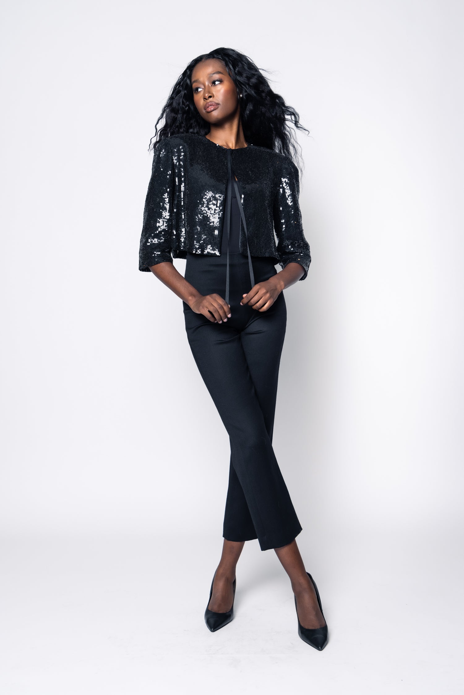 Woman wearing a black sequin jacket and black pants on a white background
