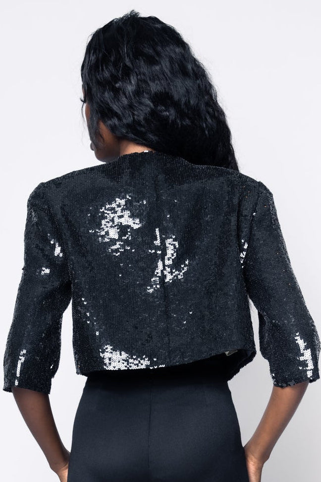 Person wearing a black sequin jacket and black pants on a white background