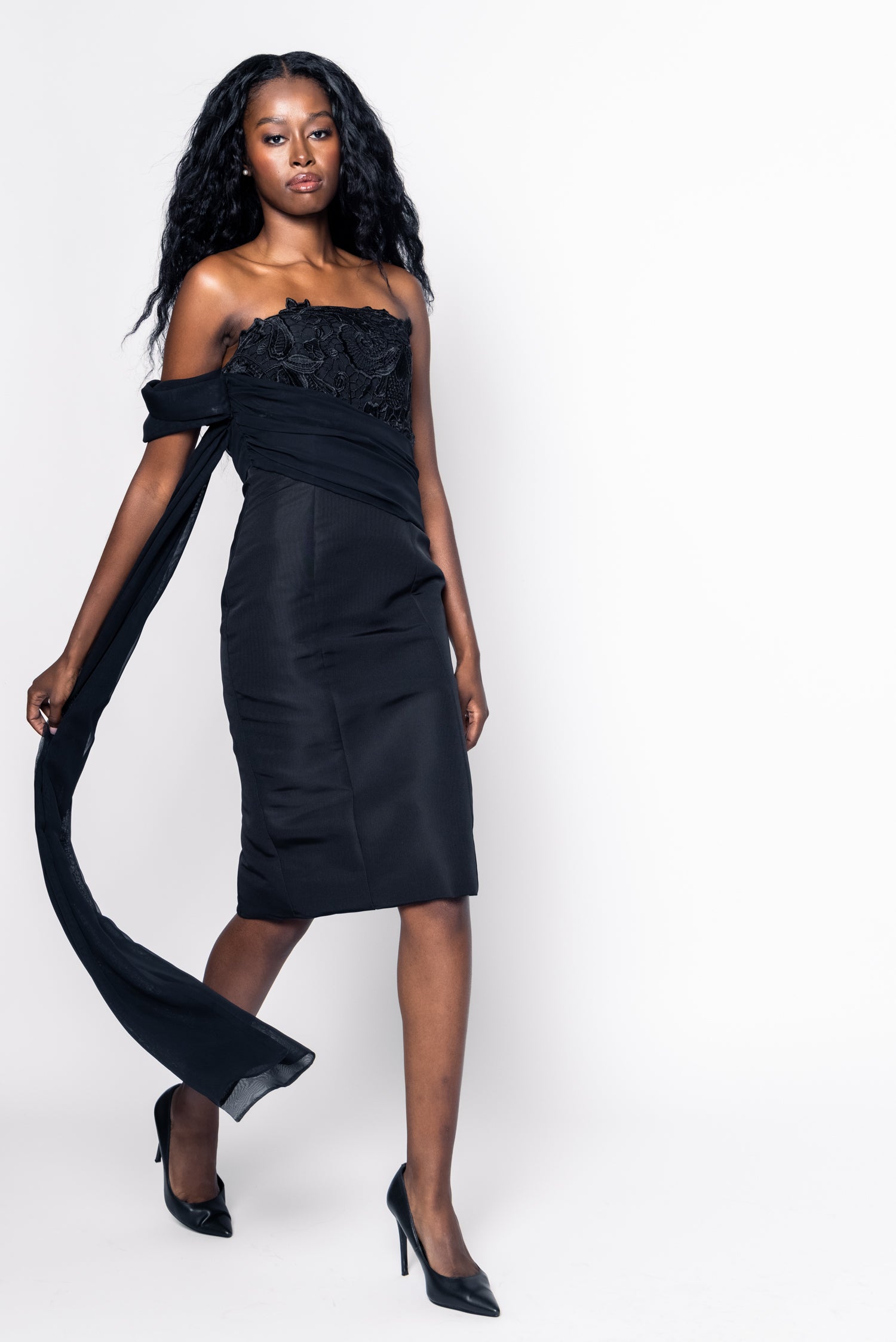 Woman wearing a black one-shoulder dress with a long train on a white background