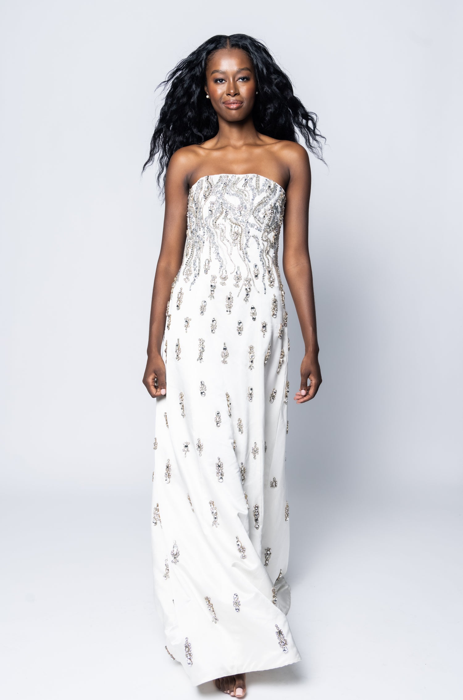 Woman wearing a strapless white dress with floral patterns on a plain background
