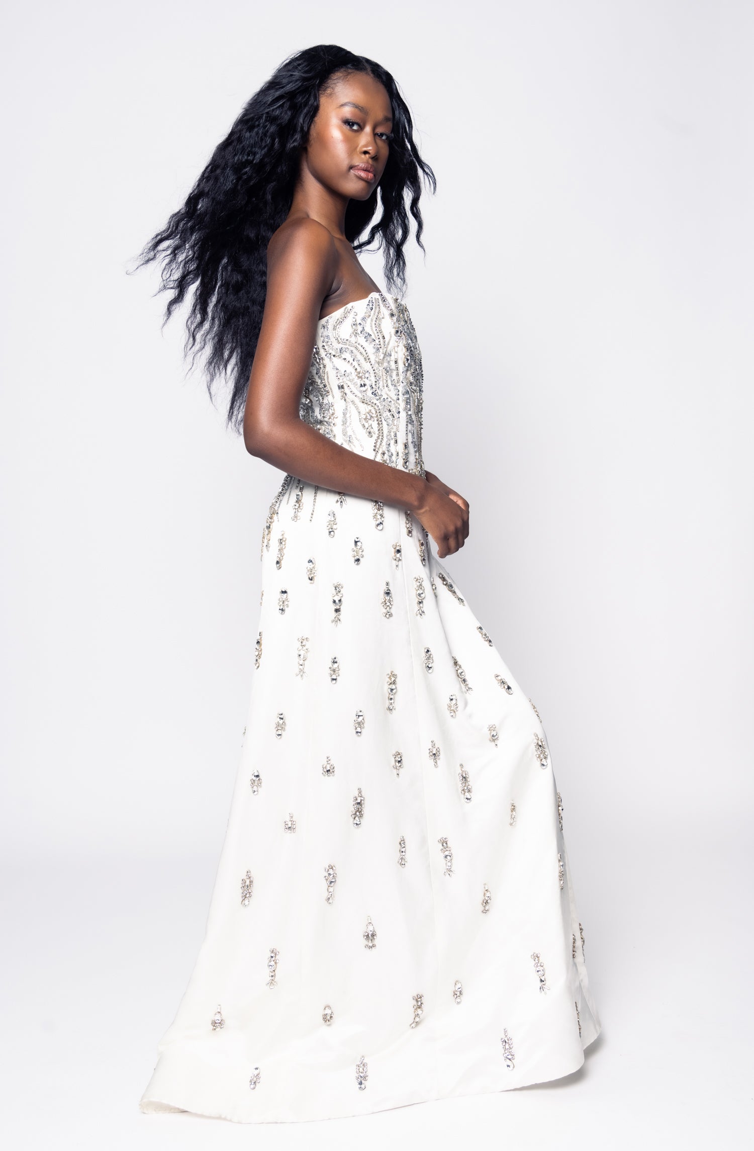 Woman wearing an off-white dress with silver bejeweled patterns on a white background