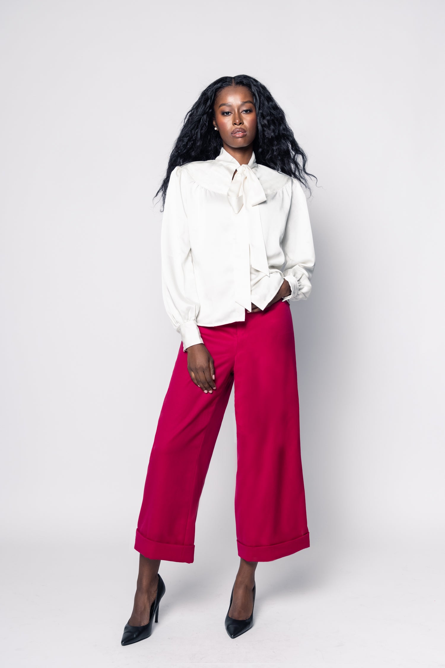 Woman wearing a white blouse with a bow tie and red pants on a white background