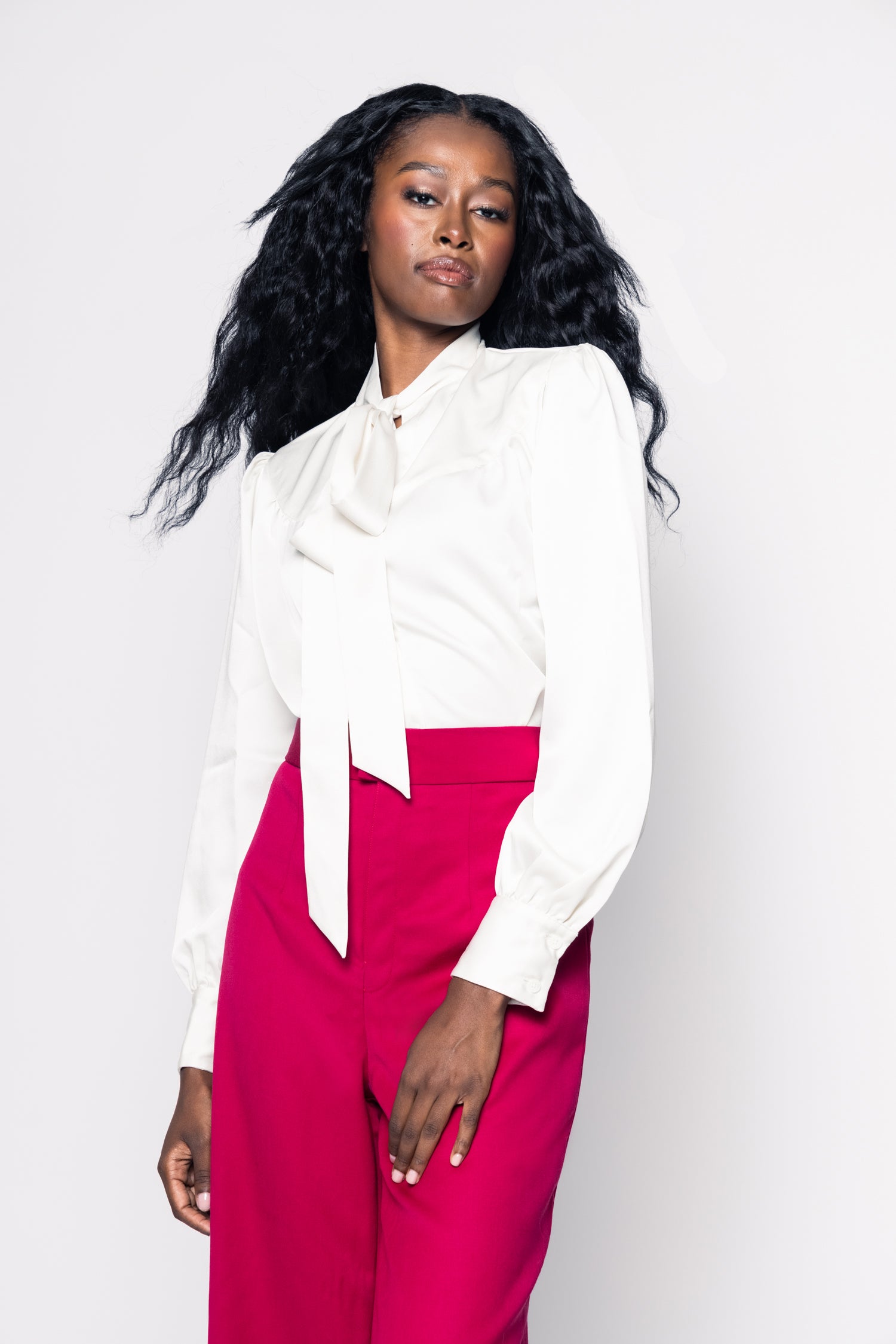 Woman wearing a white blouse with a bow tie and red pants on a white background