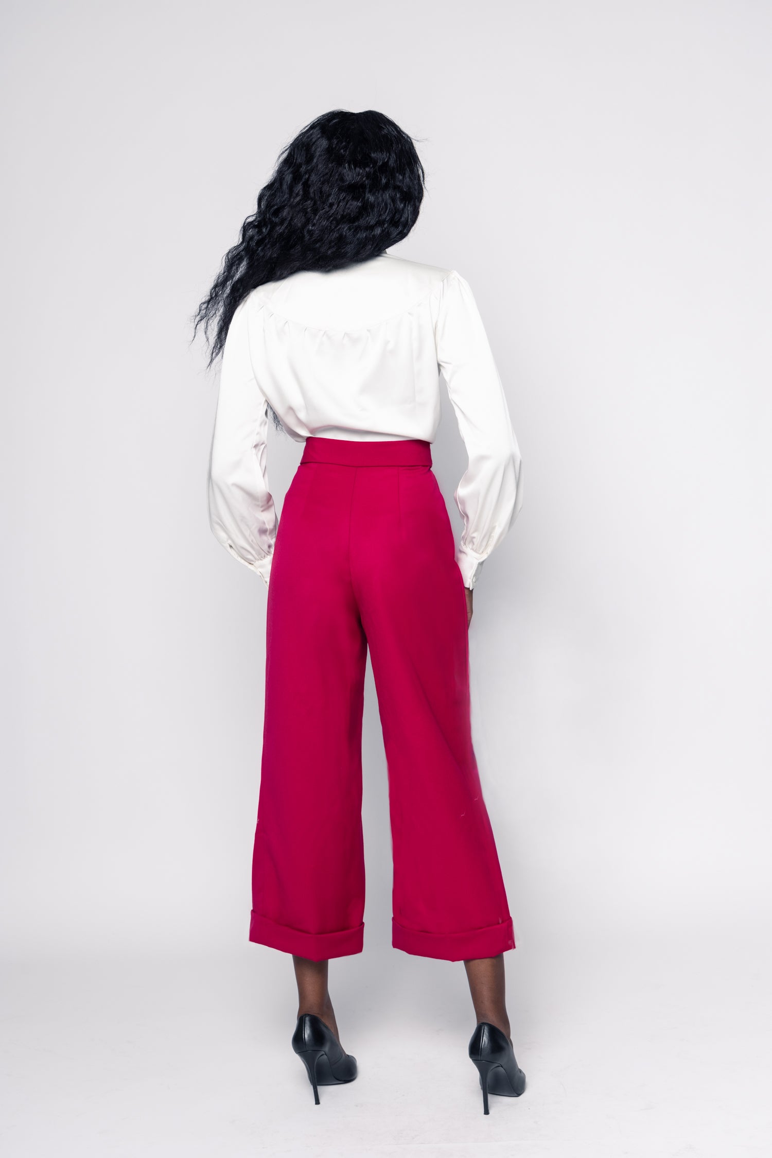 Woman wearing a white blouse with a bow tie and red pants on a white background