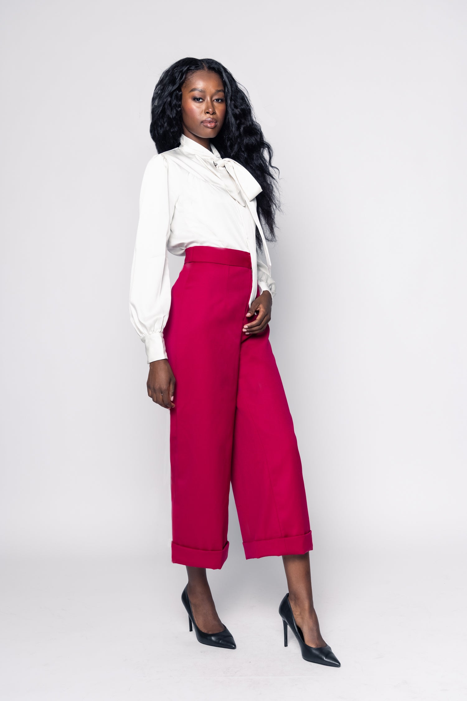 Woman wearing a white blouse with a bow tie and red pants on a white background