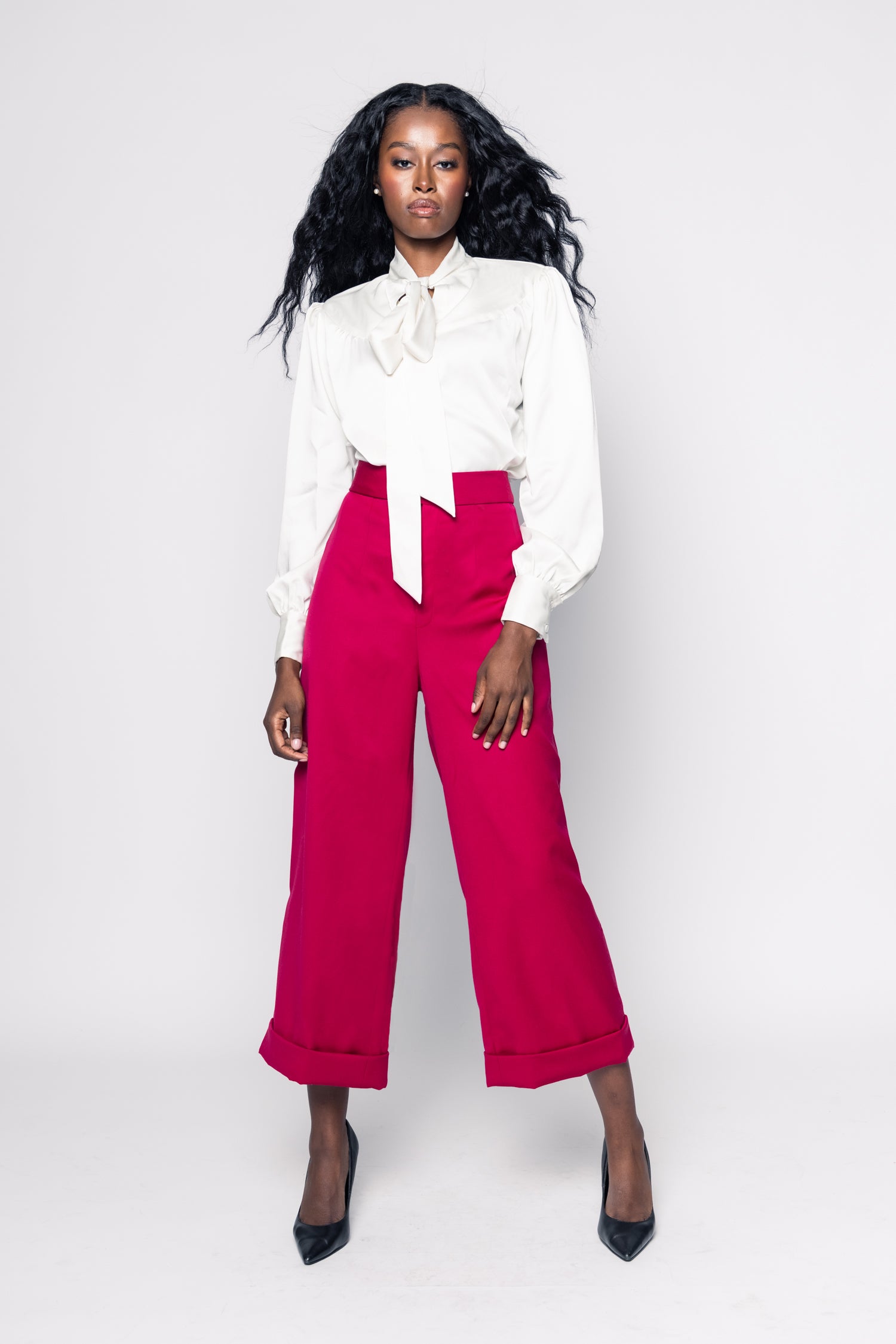 Woman wearing a white blouse with a bow tie and pink pants on a white background