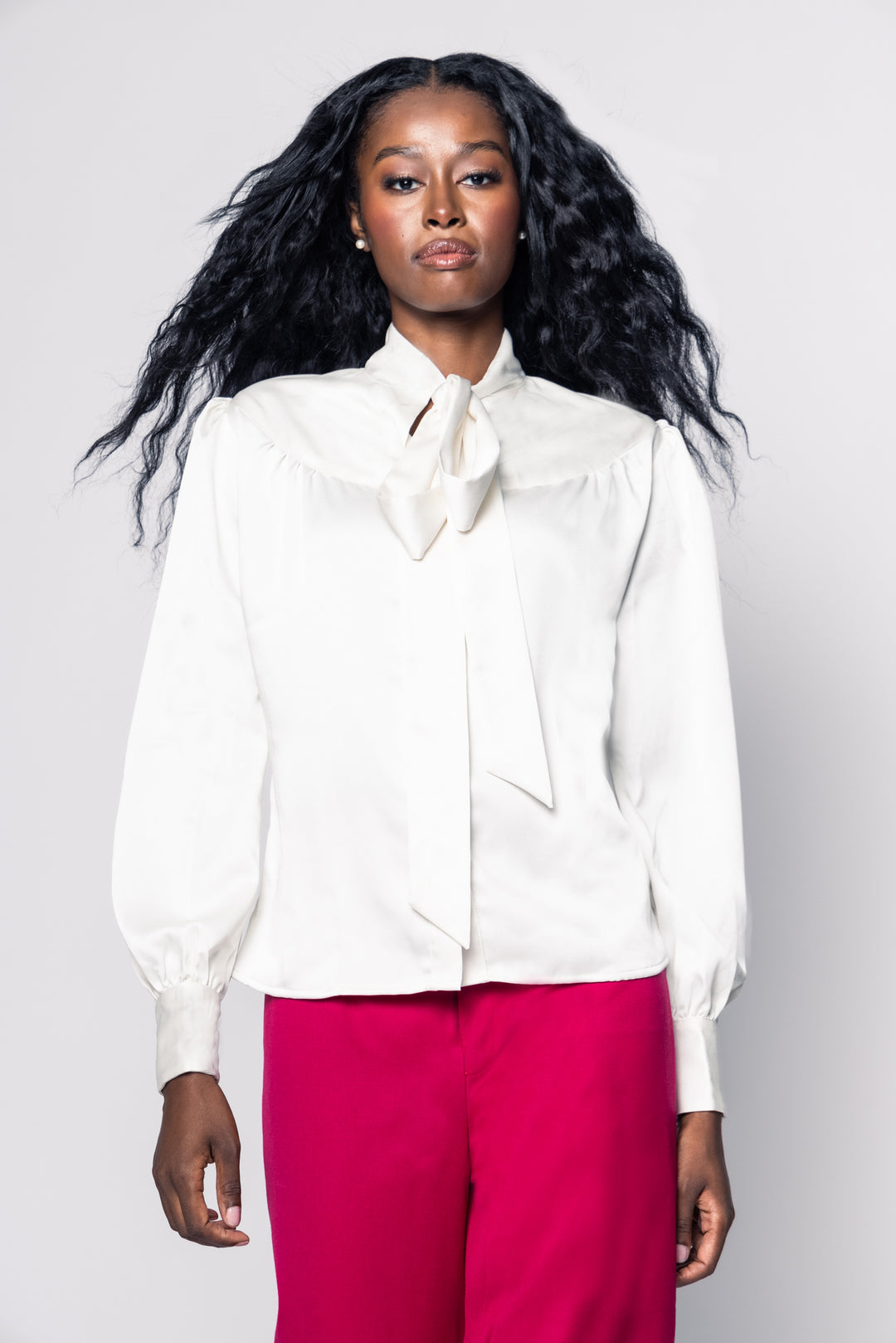 Woman wearing a white blouse with a bow tie and pink pants on a plain background