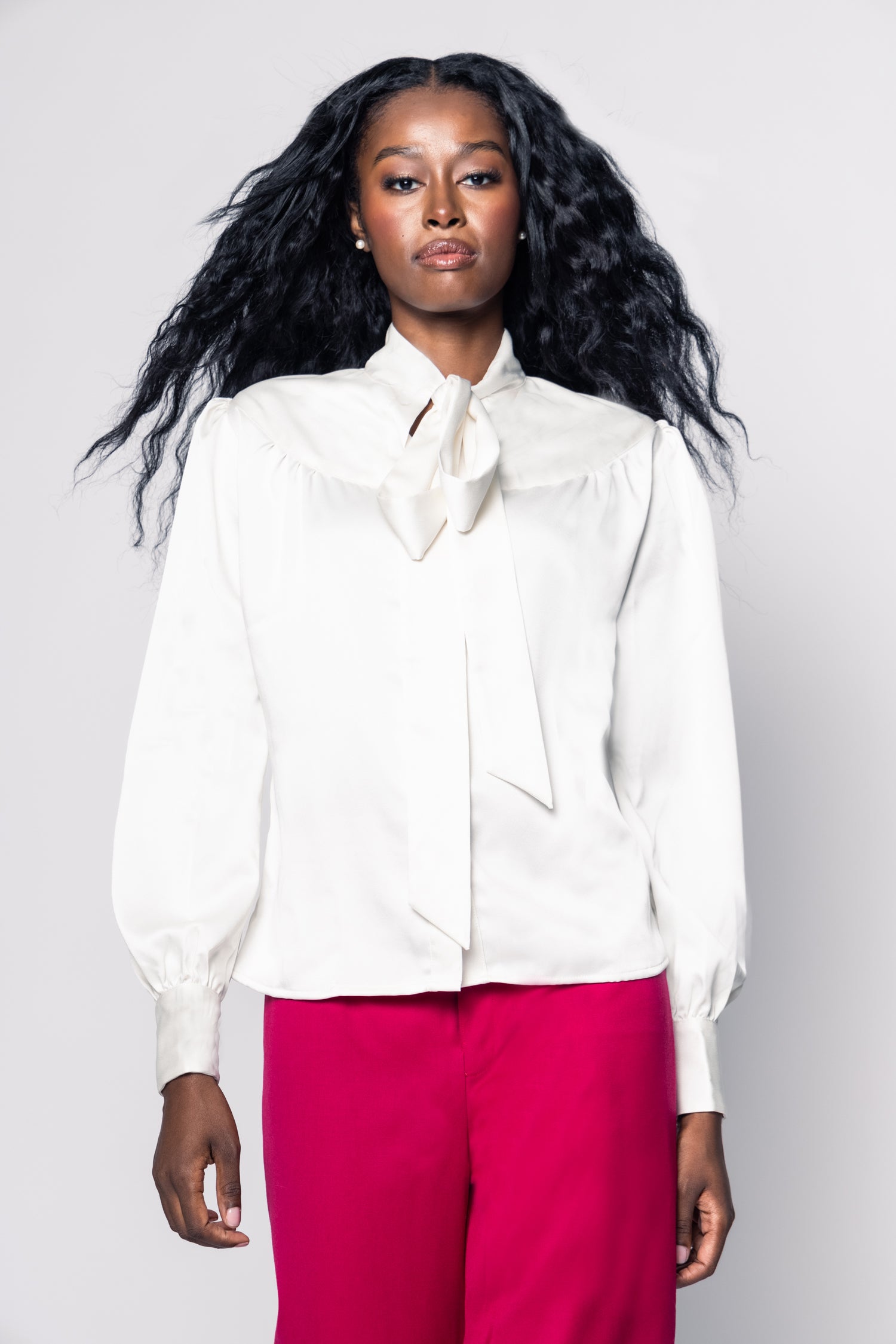 Woman wearing a white blouse with a bow tie and pink pants on a plain background