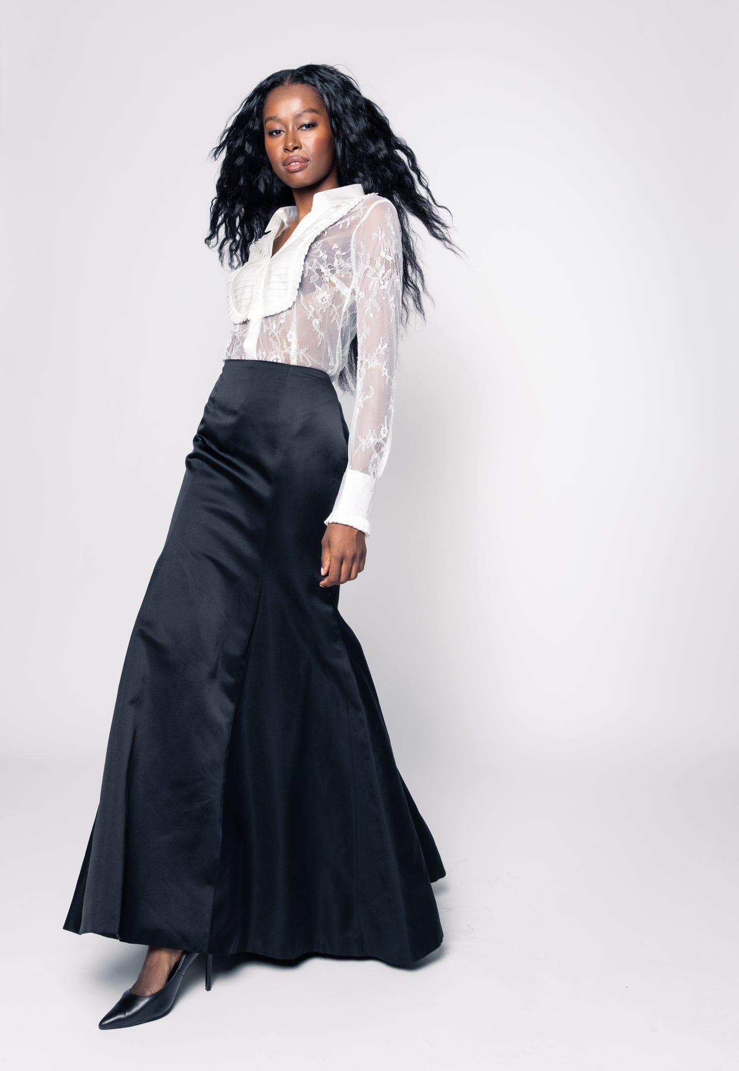 Woman wearing a black skirt and white blouse with sheer overlay on a white background