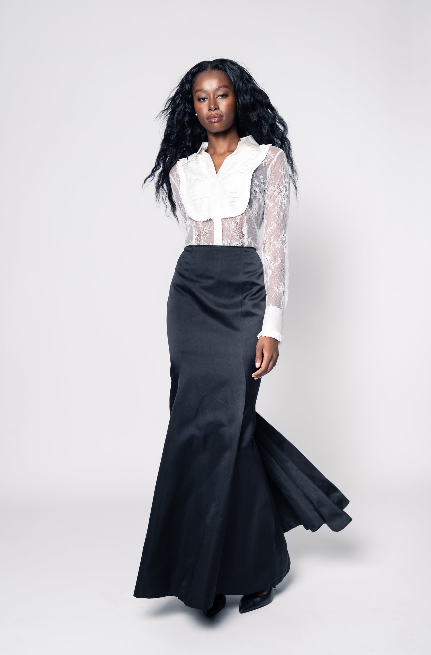 Woman wearing a black skirt and white blouse with ruffled collar on a white background