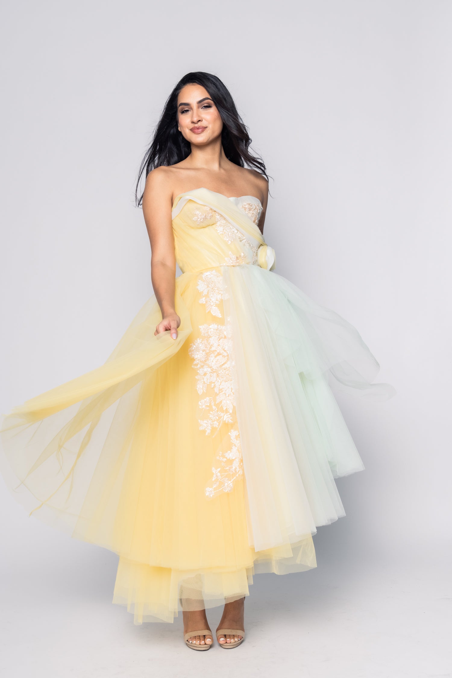 Woman wearing a yellow and white strapless gown with floral details on a plain background