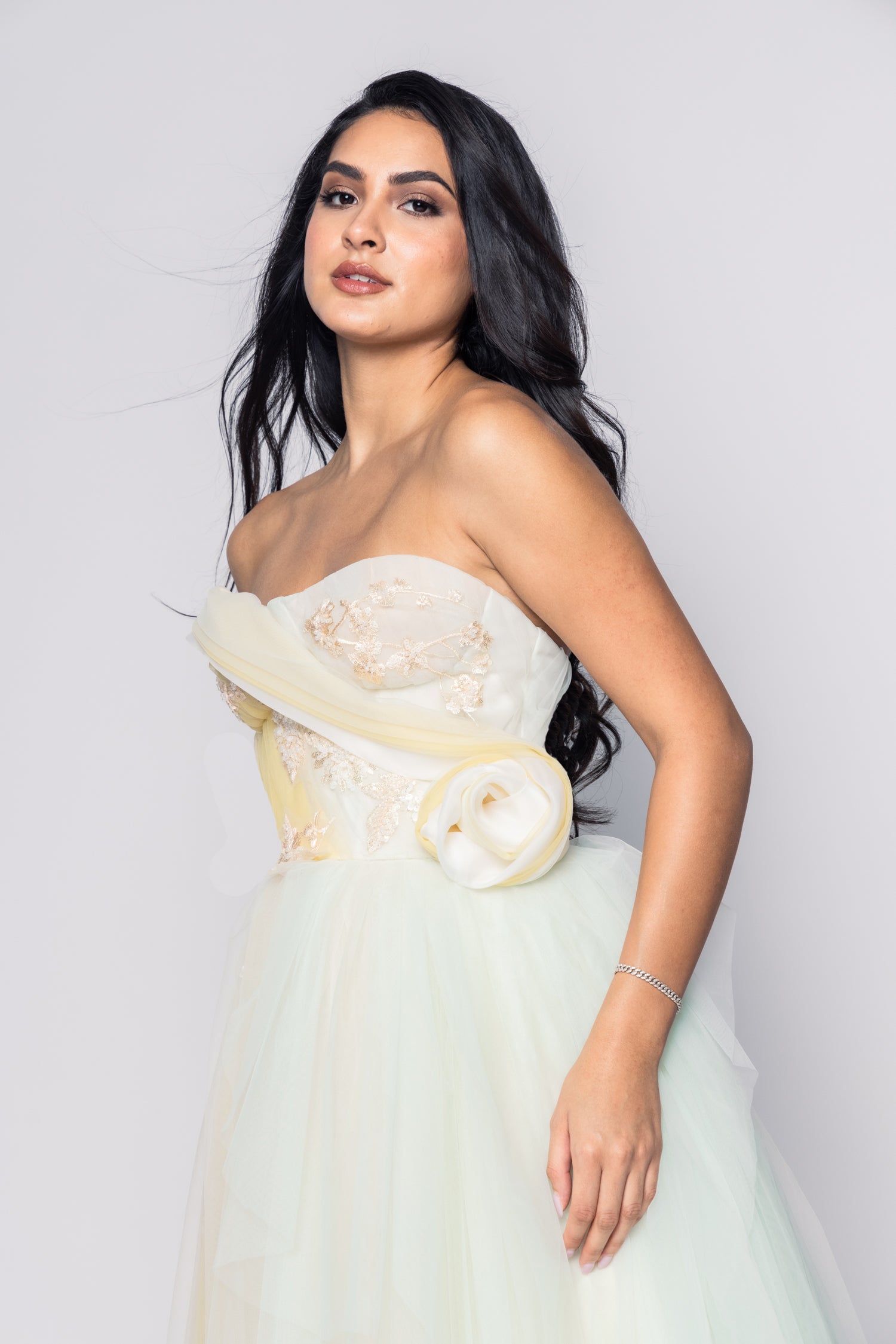 Woman wearing a strapless white dress with floral details on a plain background