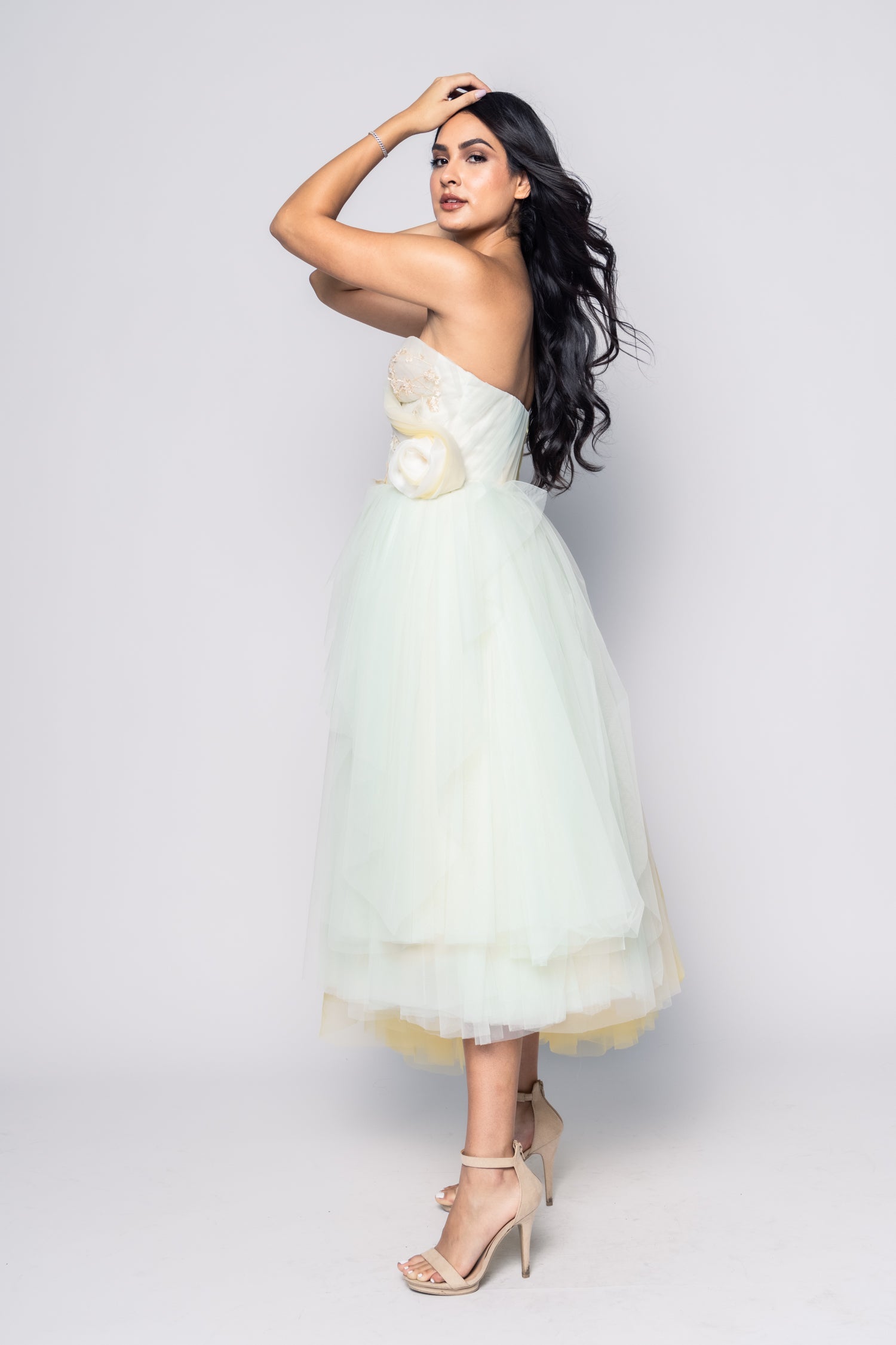 Woman wearing a light green strapless dress with floral details on a white background