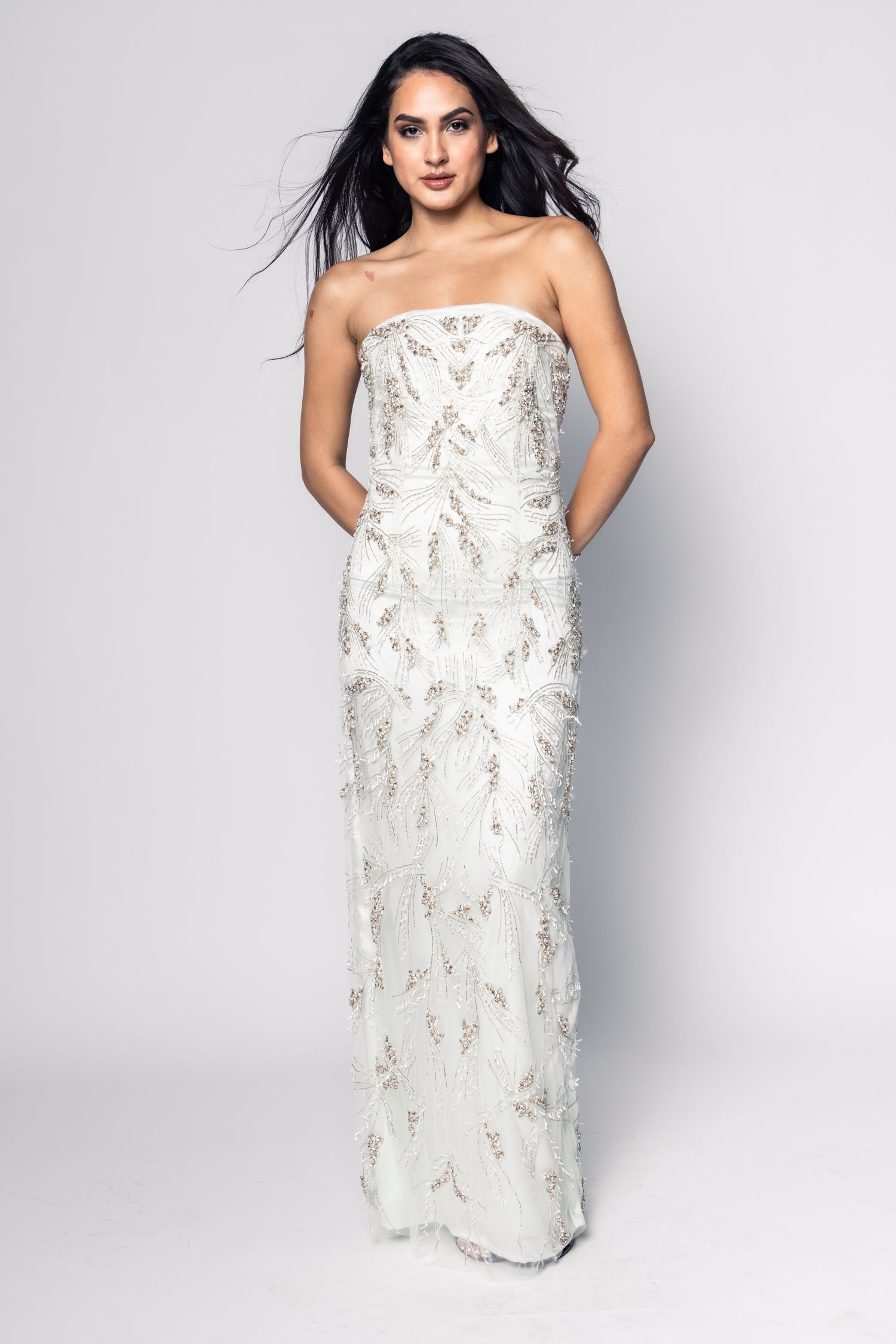 Woman wearing a strapless white gown with floral embroidery on a plain background