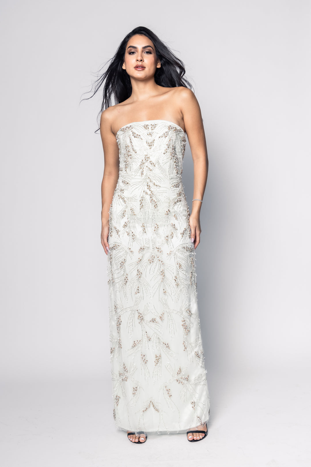Woman wearing a strapless, long, white embroidered dress against a plain background