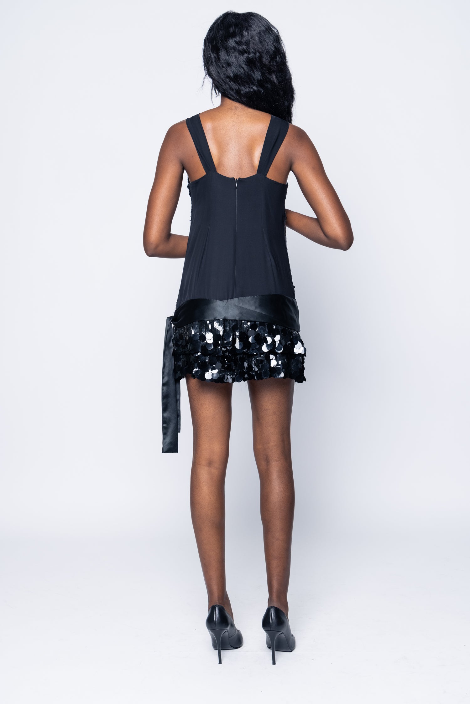 Person wearing a black sleeveless top and sequin skirt on a white background