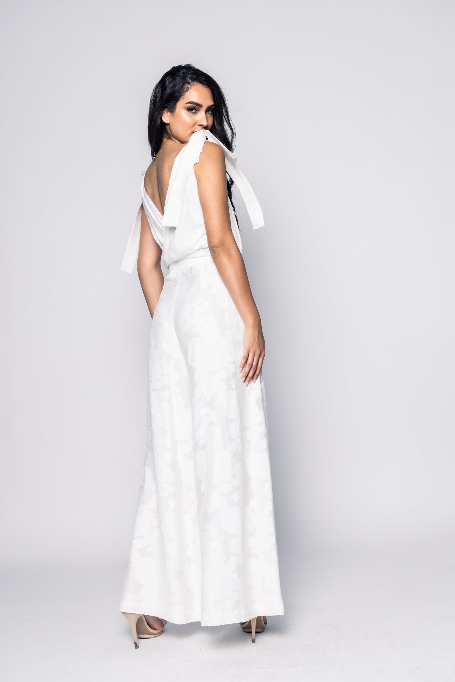 Woman wearing a white dress with ruffled sleeves against a plain background