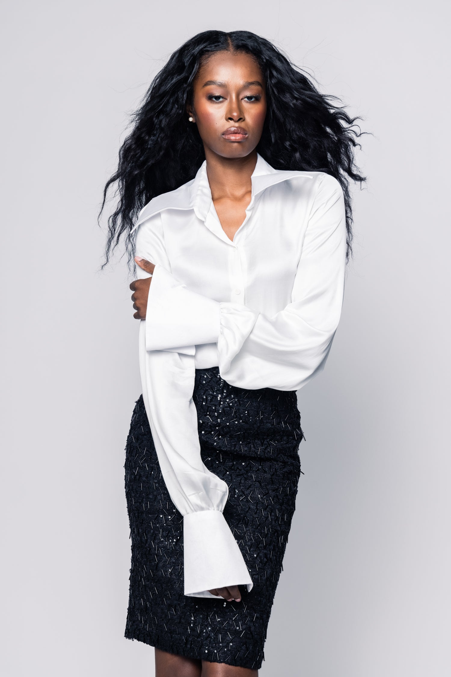 Woman wearing a white blouse and black sequin skirt against a gray background