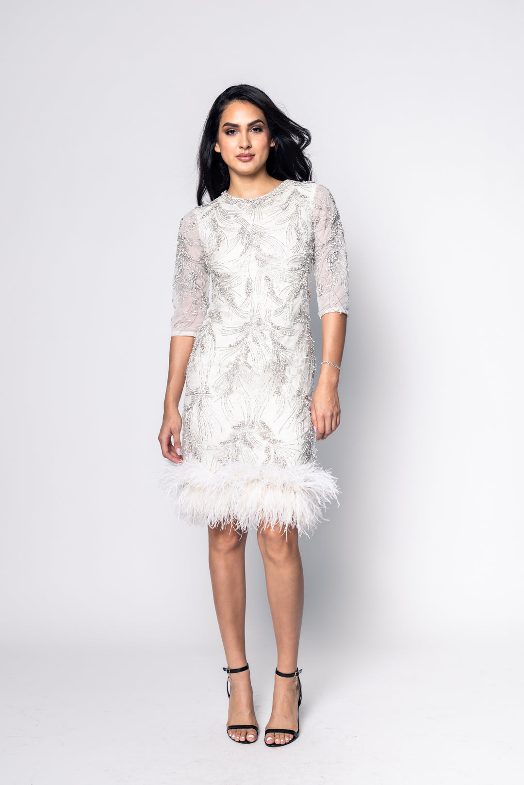 Woman wearing a white lace dress with feather details on a white background