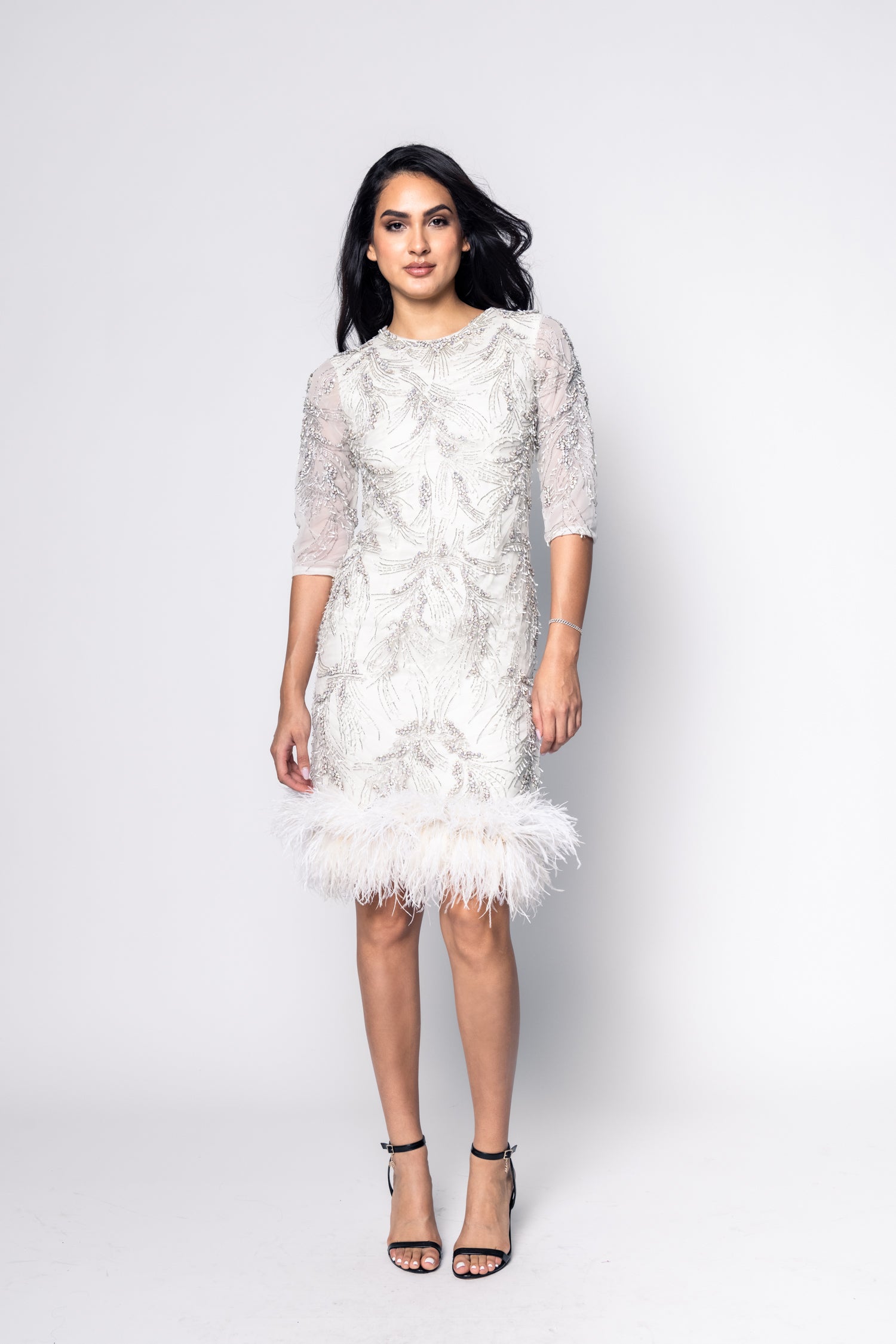 Woman wearing a white lace dress with feather details on a white background