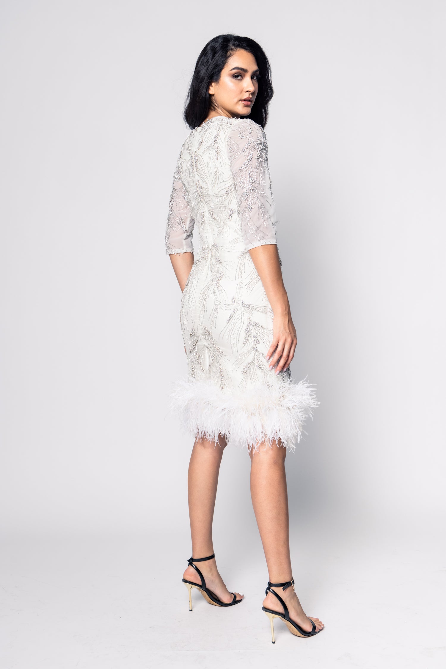 Woman wearing a white lace dress with feather details on a white background