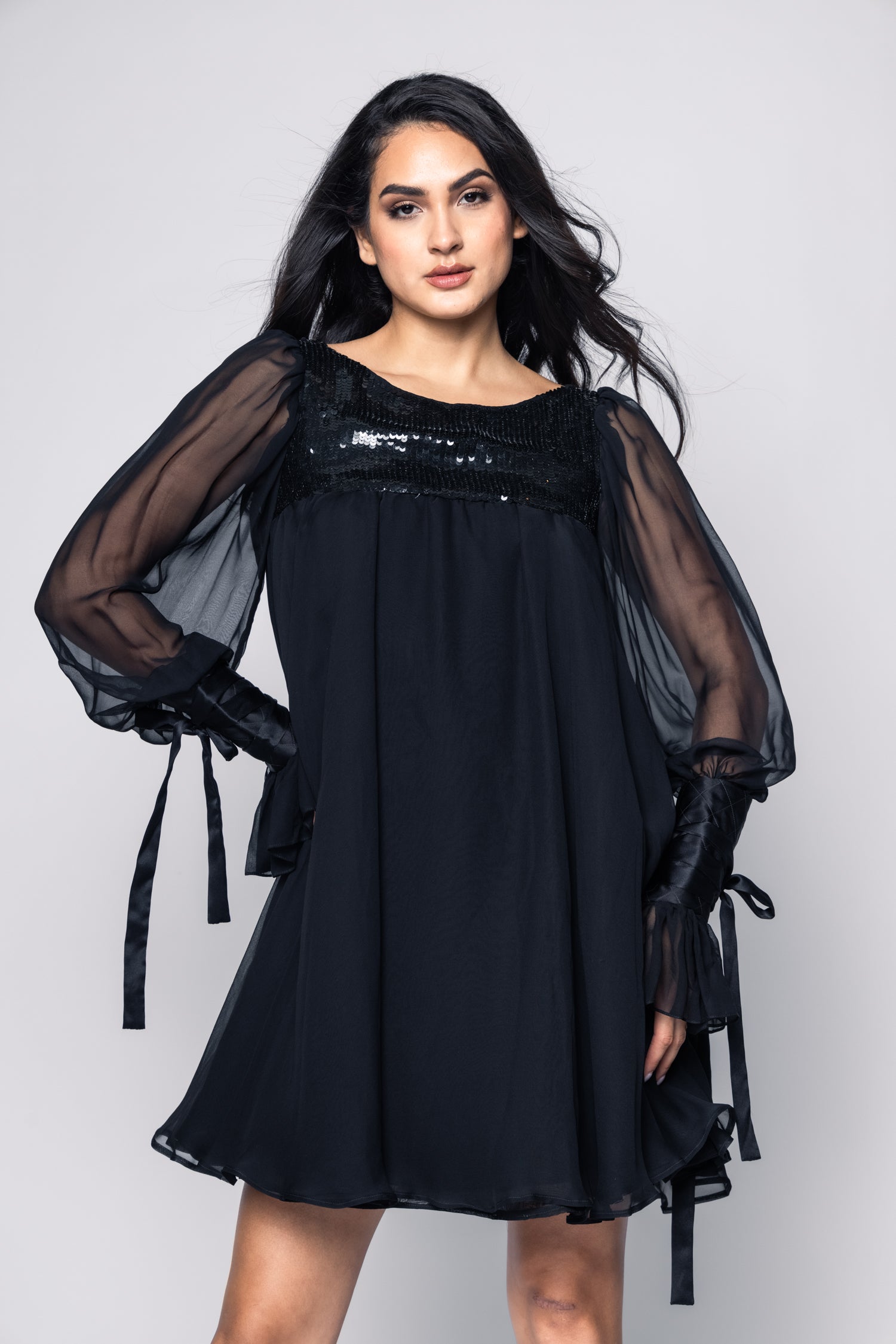 Woman wearing a black dress with sheer sleeves against a white background