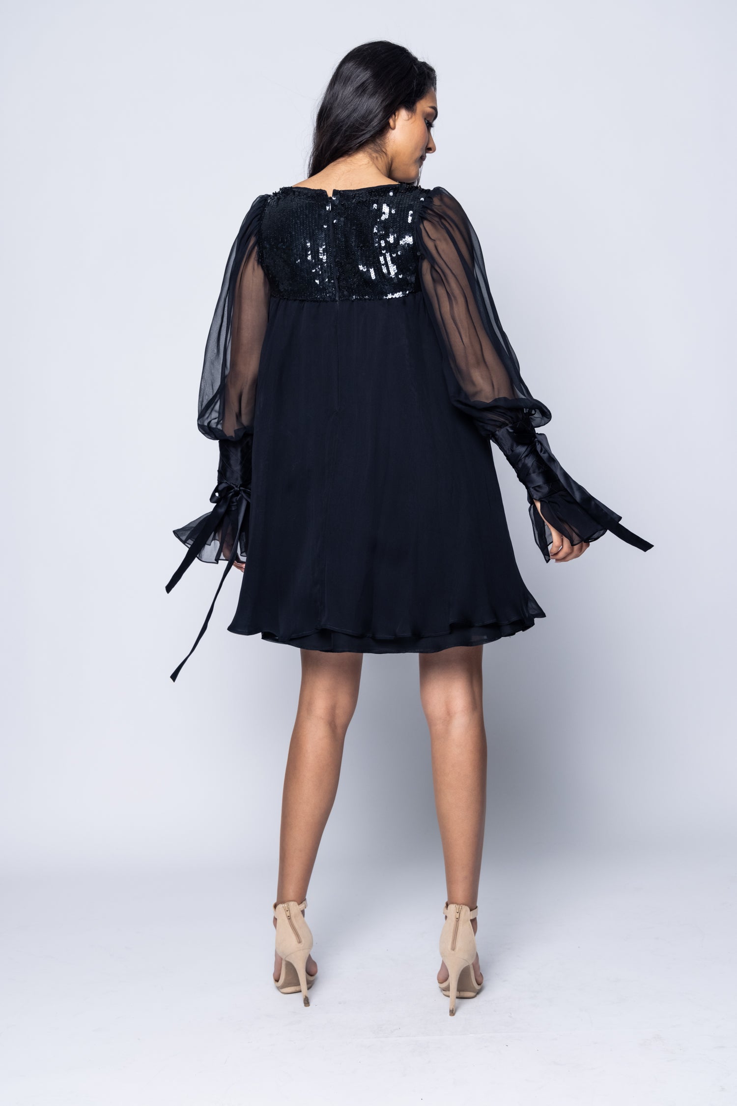Woman wearing a black dress with sheer sleeves on a white background