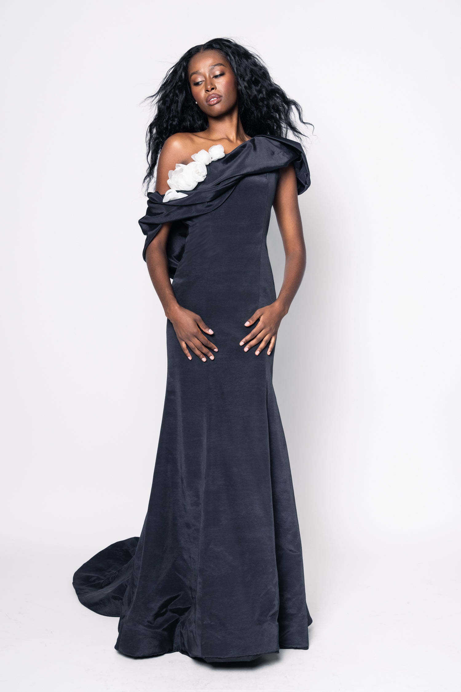 Woman wearing a black one-shoulder gown with floral details on a white background
