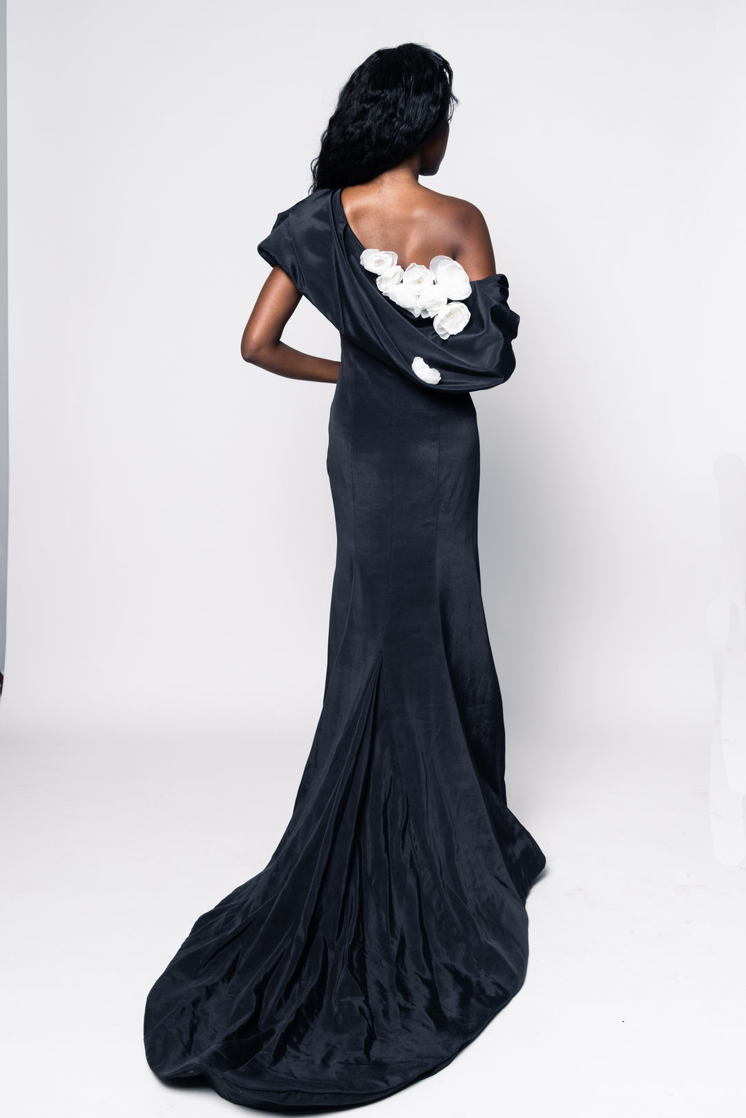 Woman wearing a black one-shoulder gown with floral details on a white background