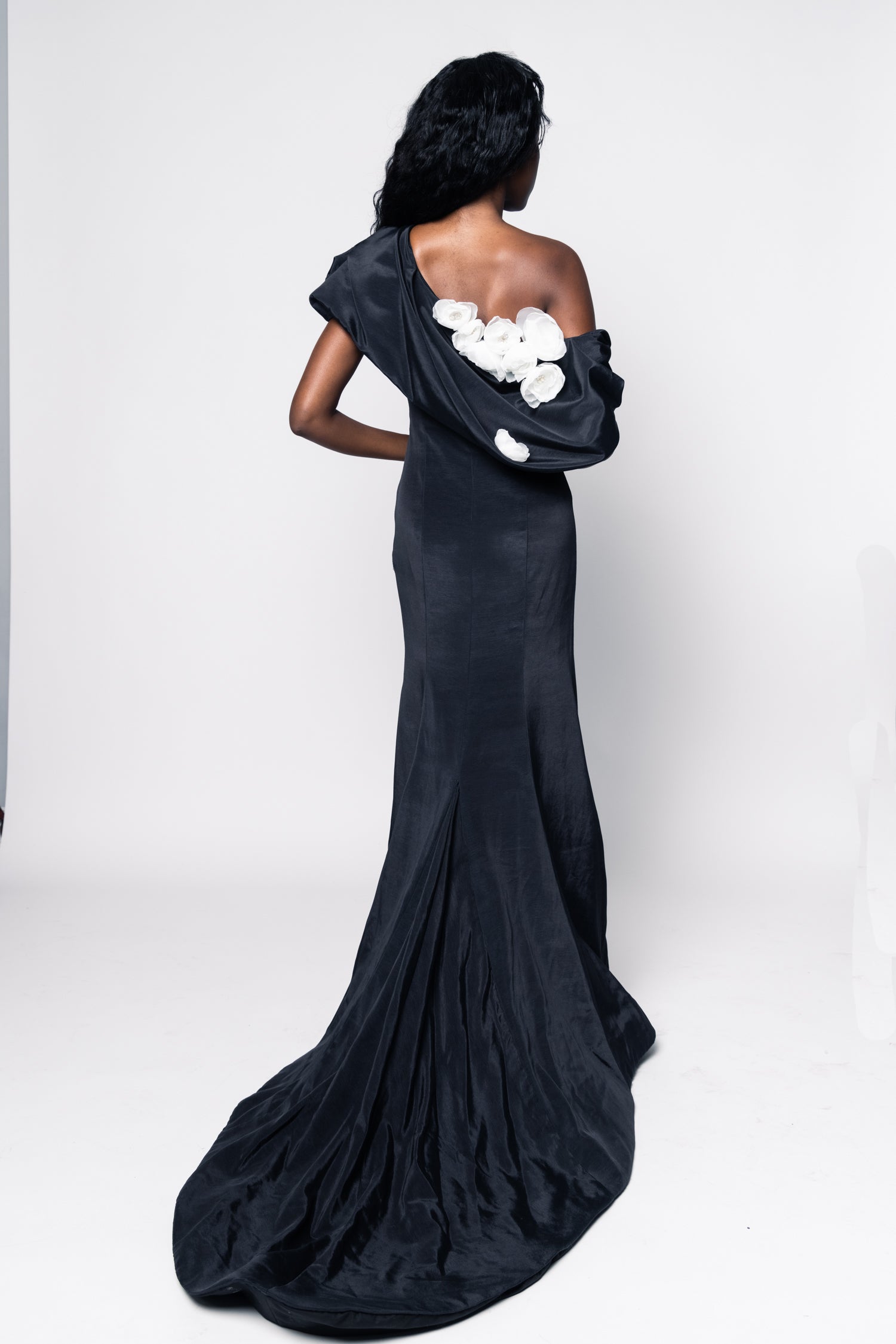 Woman wearing a black one-shoulder gown with floral details on a white background