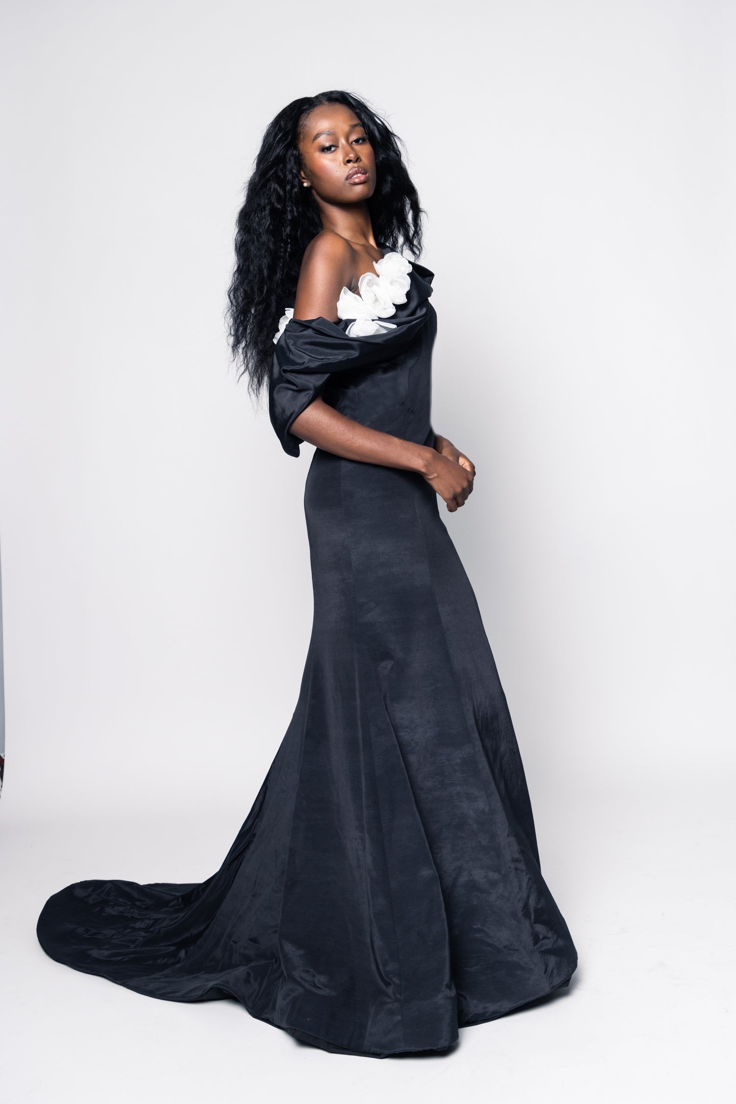 Woman wearing a long black off-shoulder dress against a white background