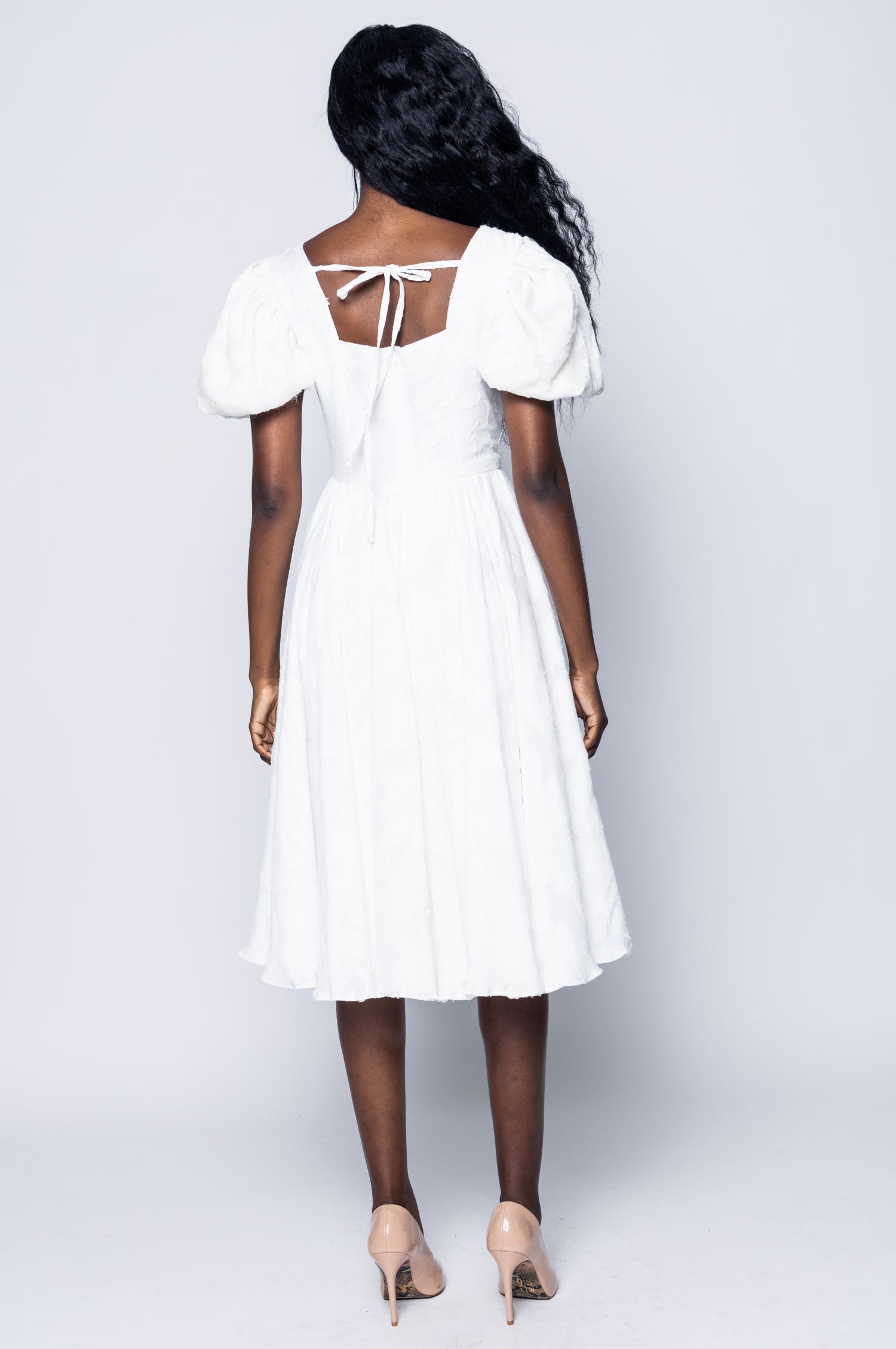 Woman wearing a white dress with puffed sleeves on a plain background