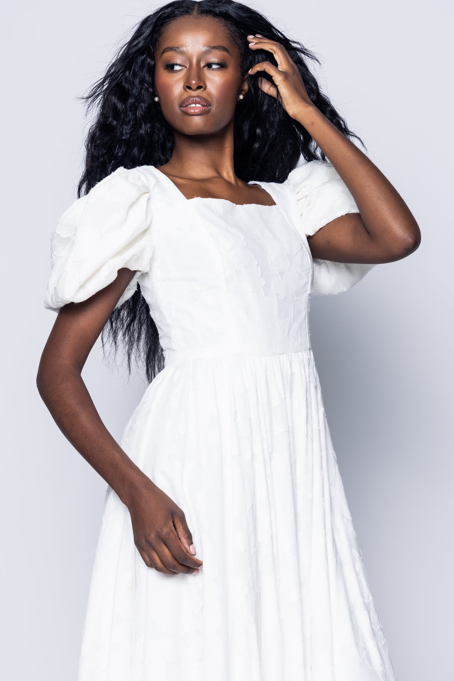 Woman wearing a white dress with puffed sleeves against a plain background