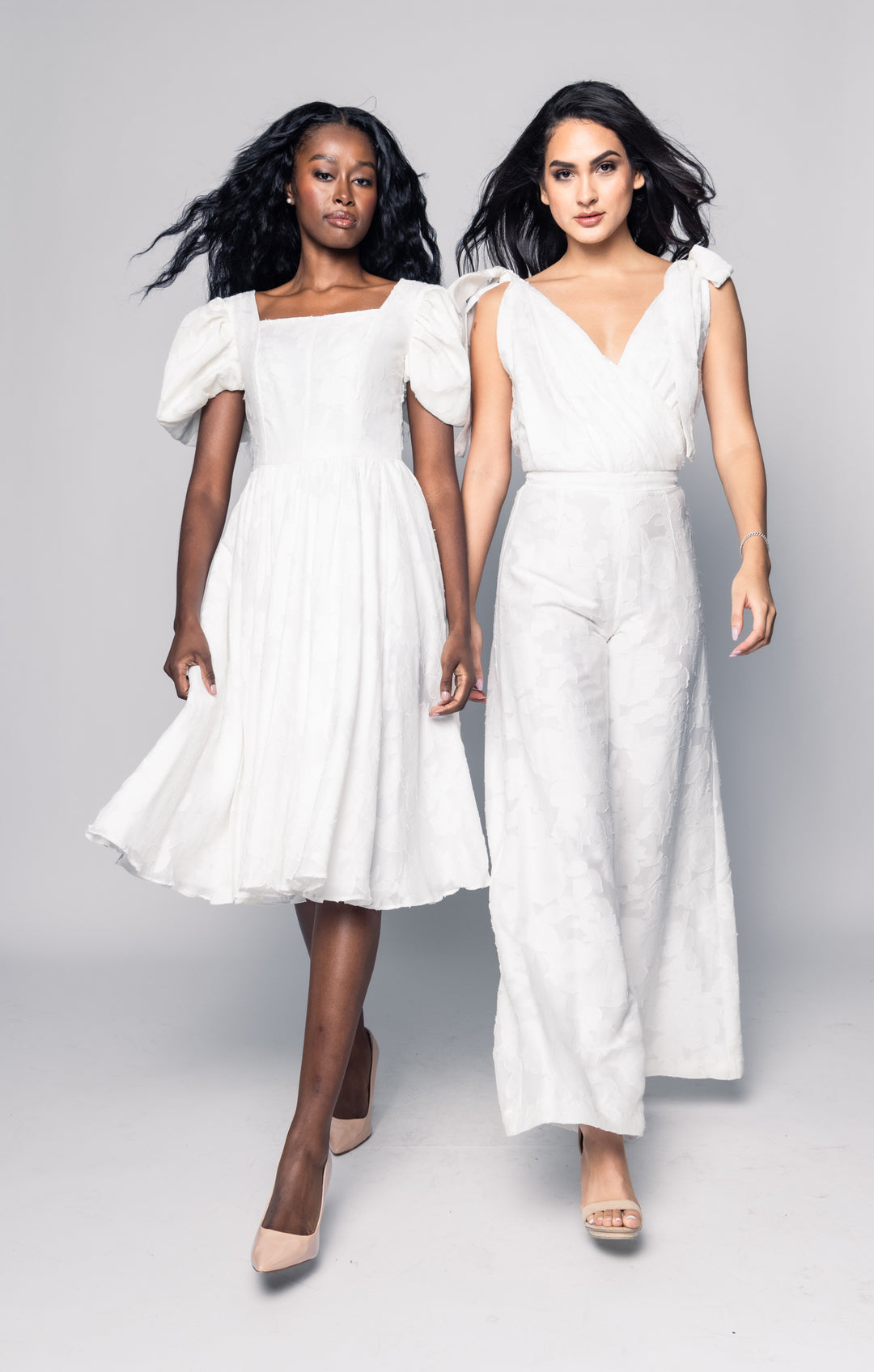 Two women wearing white dresses on a gray background
