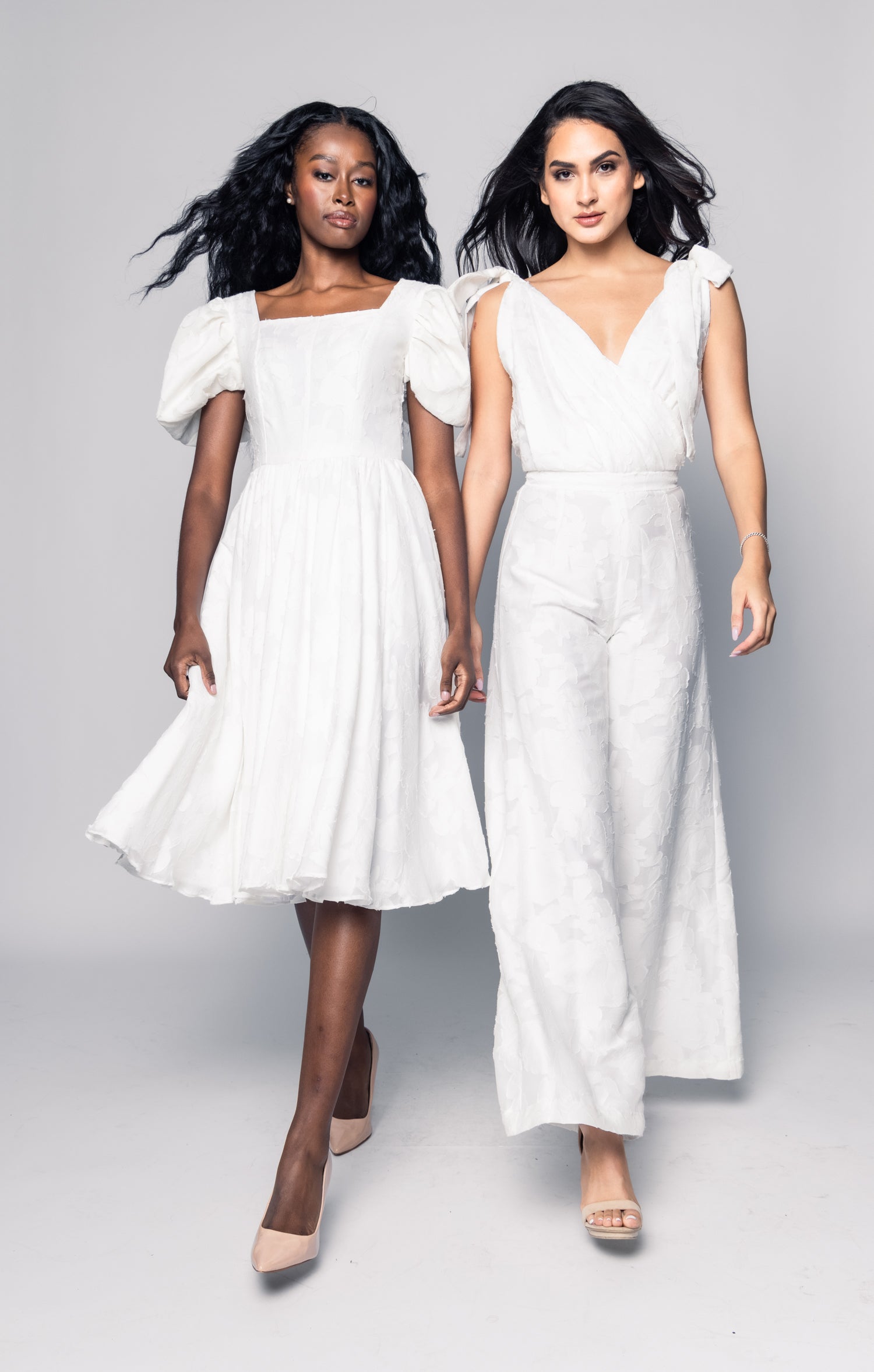 Two women wearing white dresses on a gray background