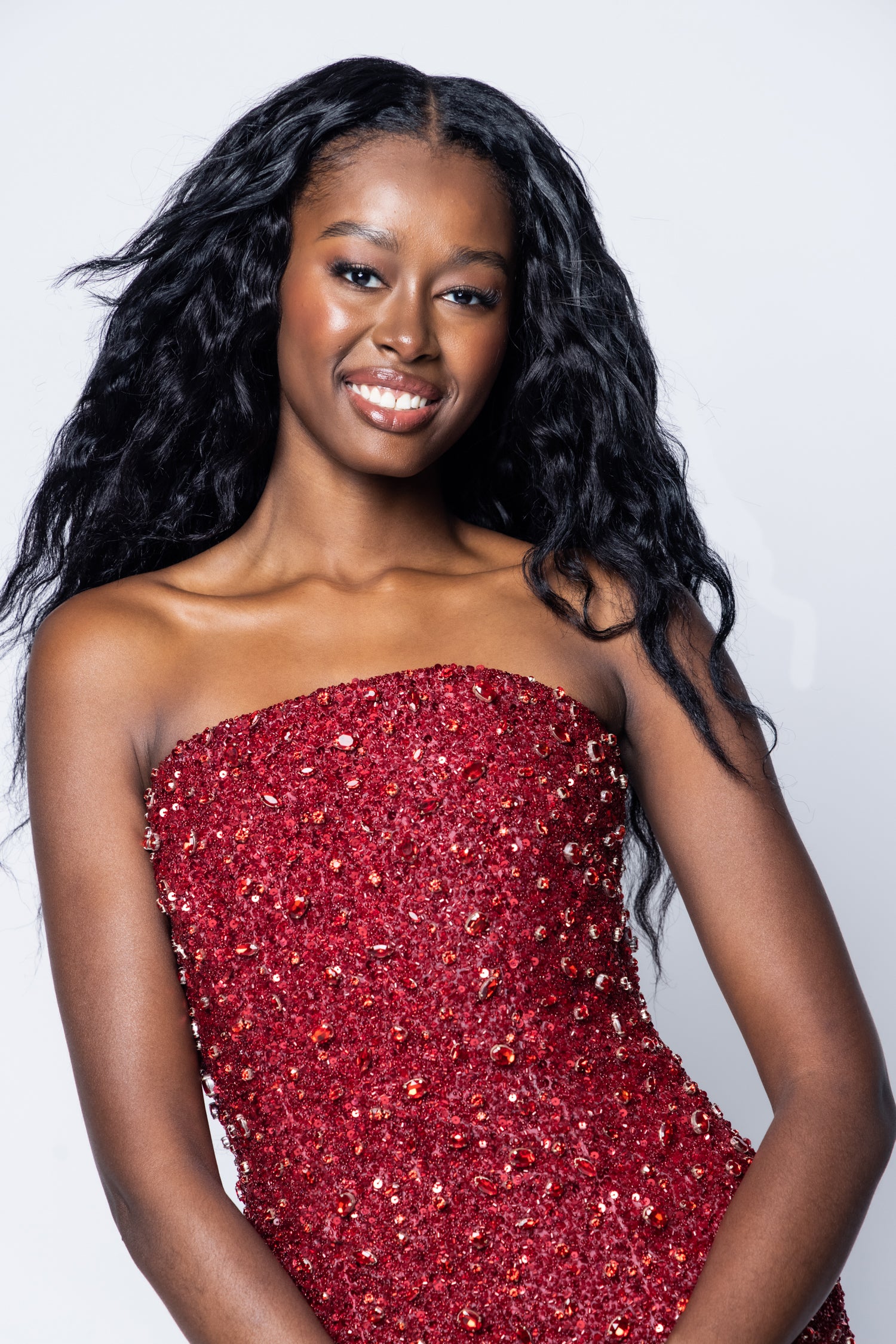 Woman wearing a red strapless dress with sequins against a plain background