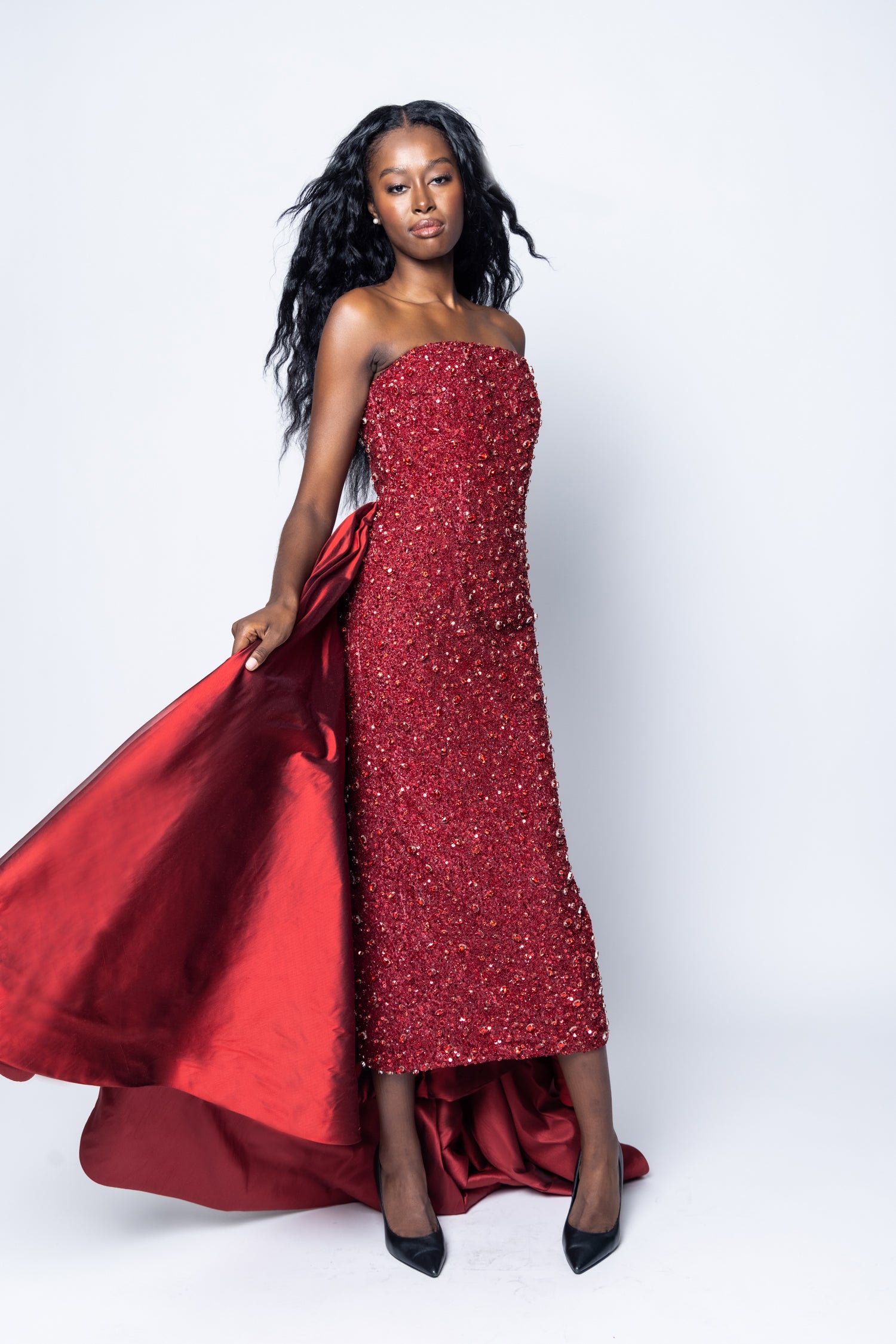 Woman wearing a red strapless gown with a large train on a white background