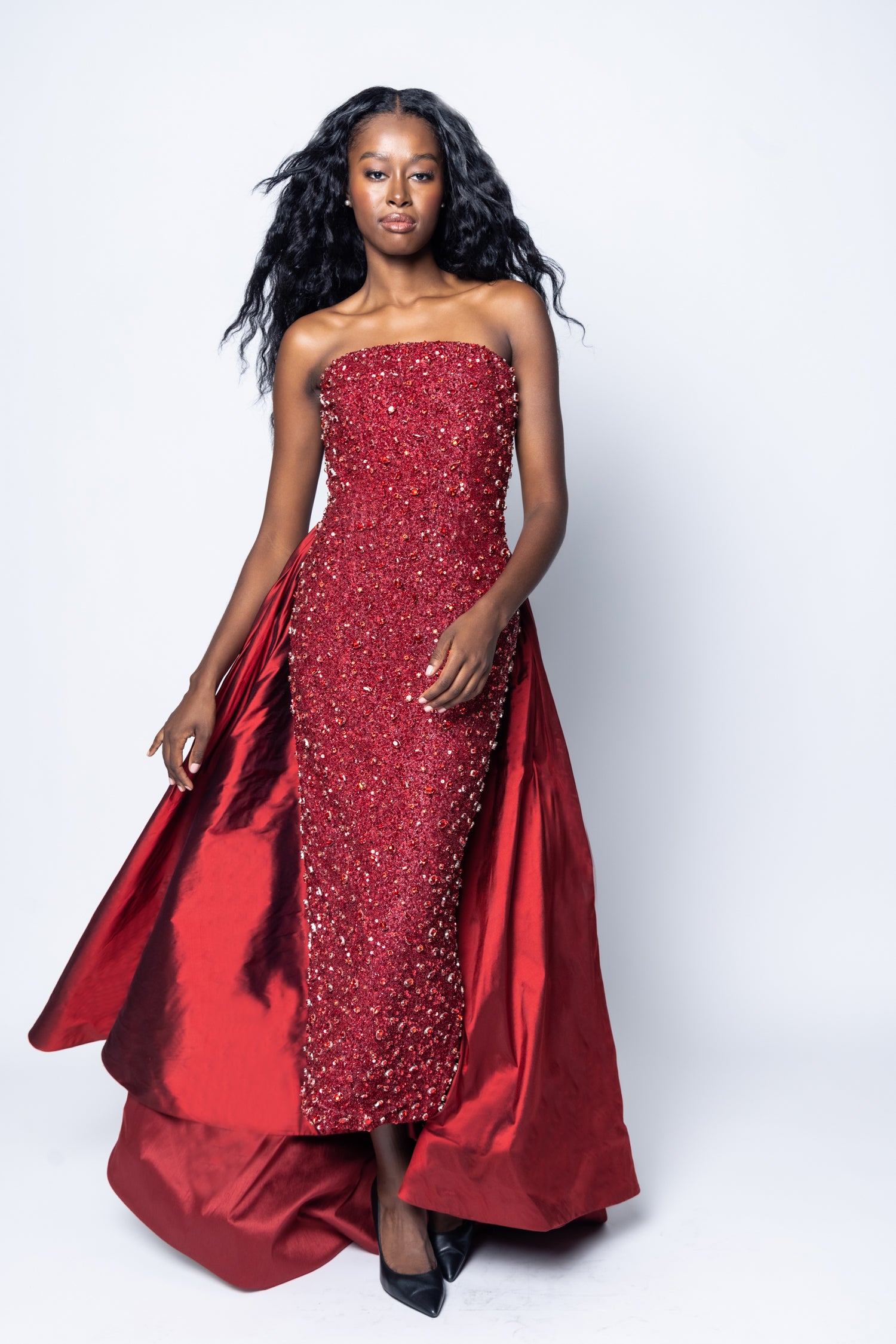 Woman wearing a red strapless gown with beading on a white background