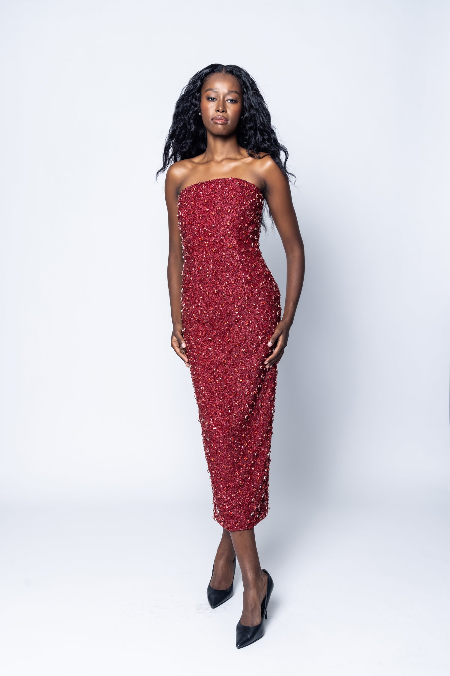 Woman wearing a red strapless dress with black heels on a white background