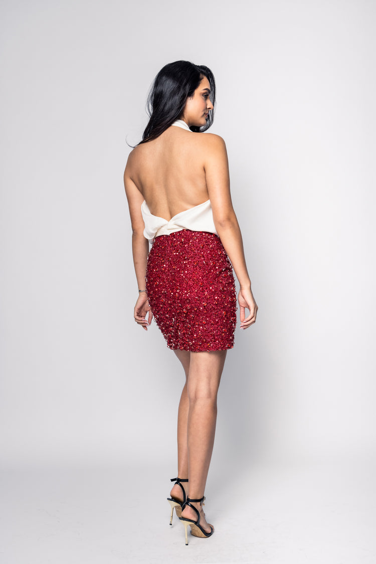 Woman wearing a red sequin skirt and white top on a plain background